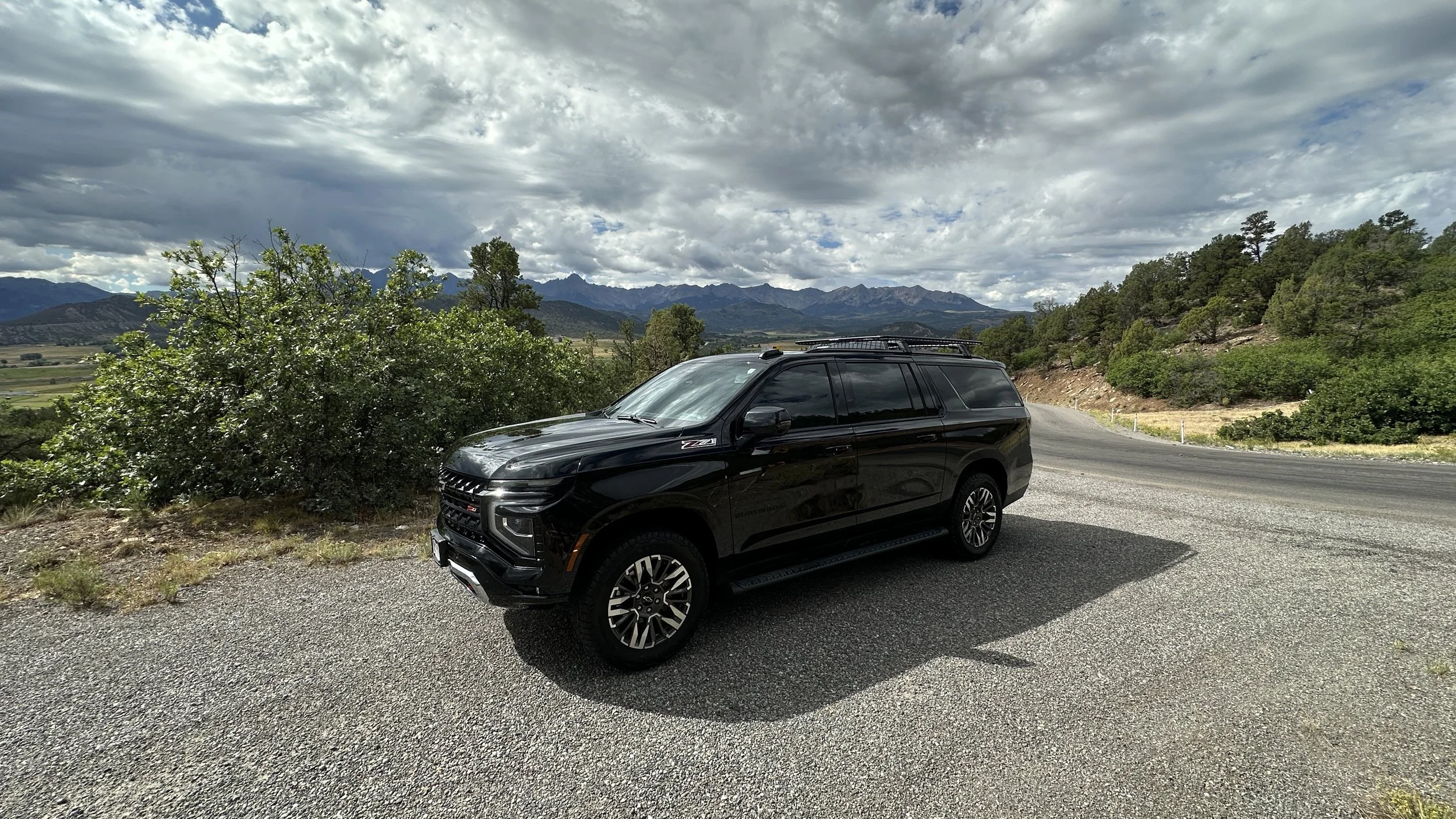 Luxury black Suburban parked on a Telluride roadside with a large mountain range in the background.