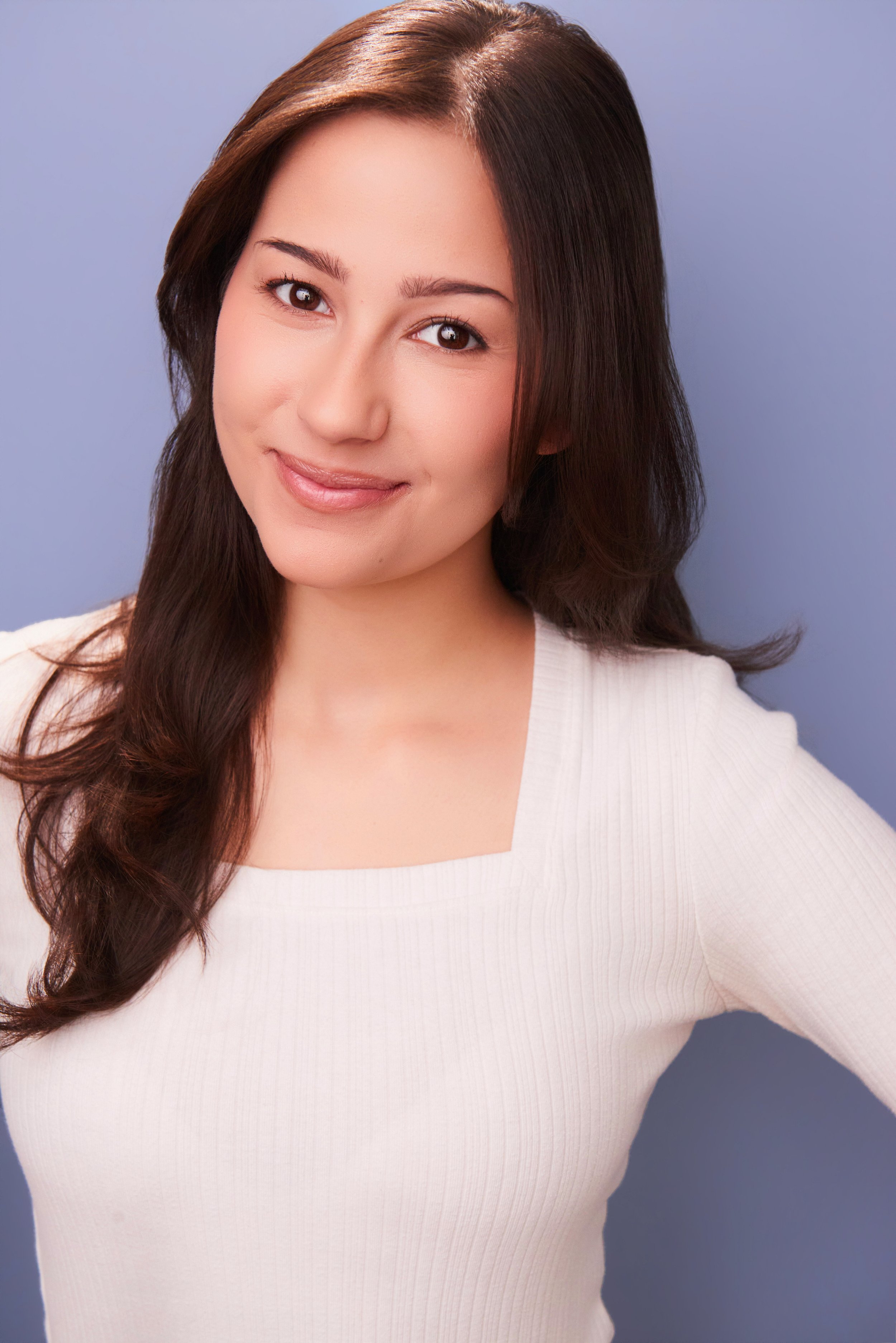 A woman with long brown hair and a white top standing against a light blue background.