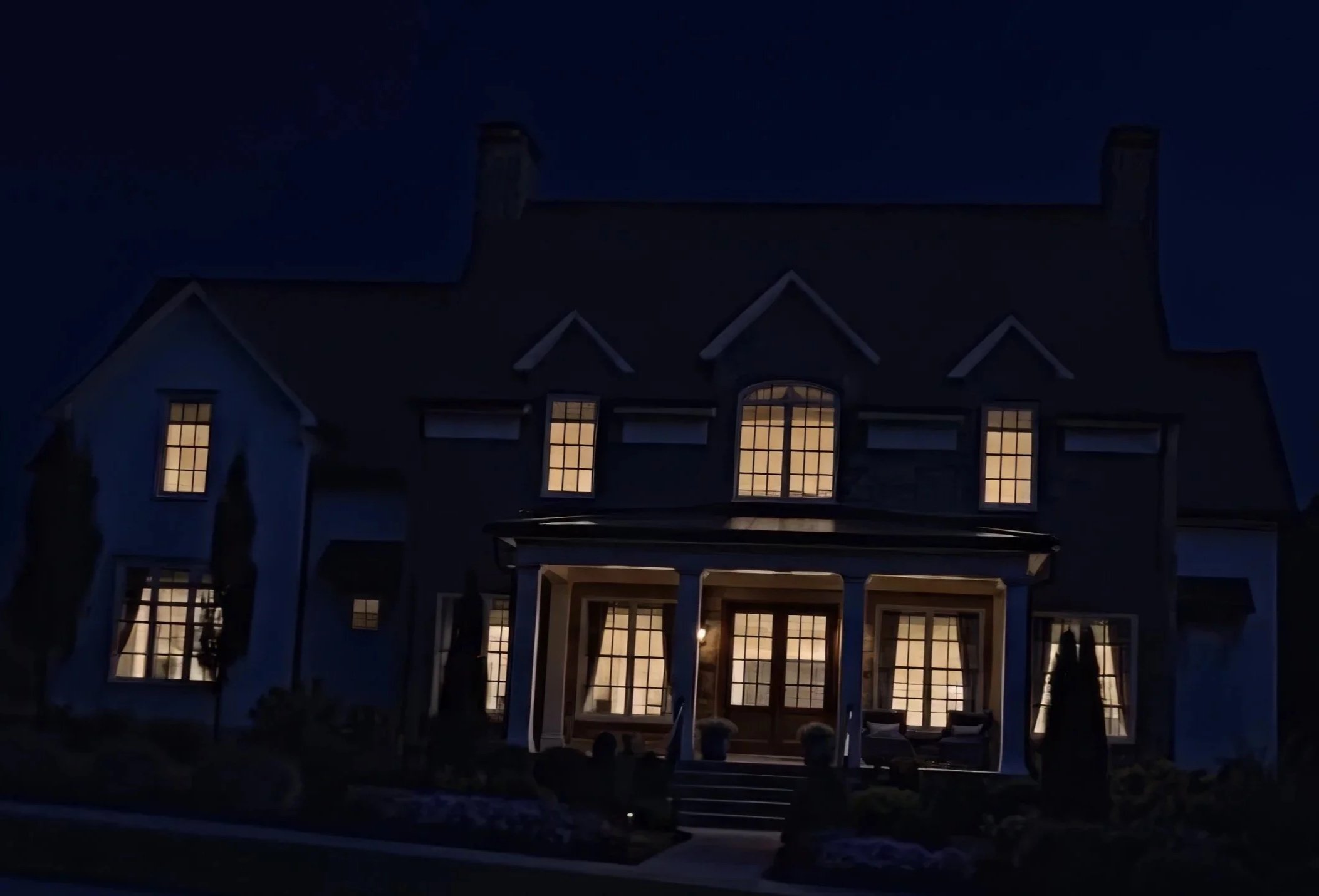 Large stately house with warmly lit windows and covered entrance at night