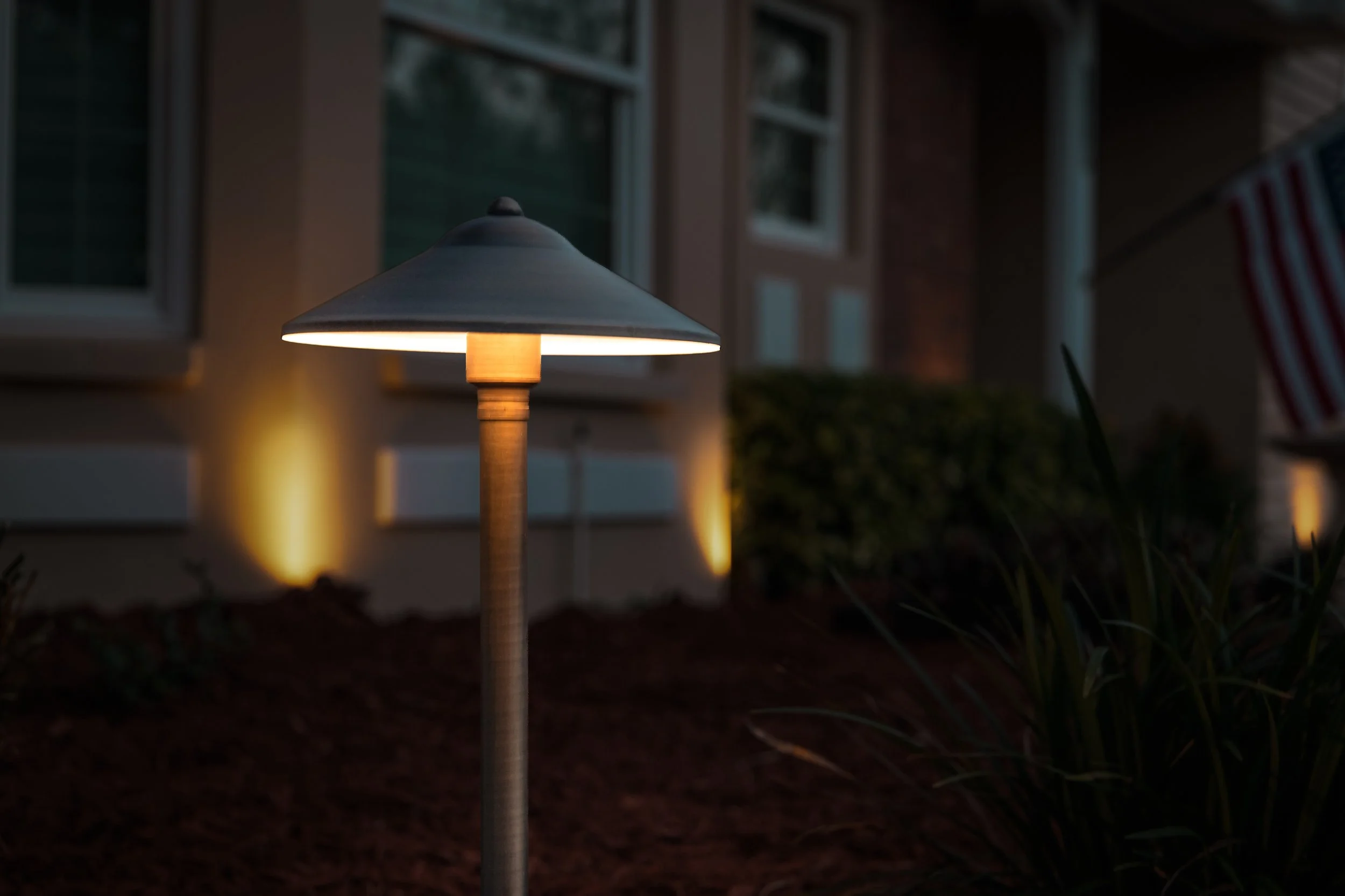 Glowing outdoor pathway lamp illuminating landscaping in front of a building at dusk