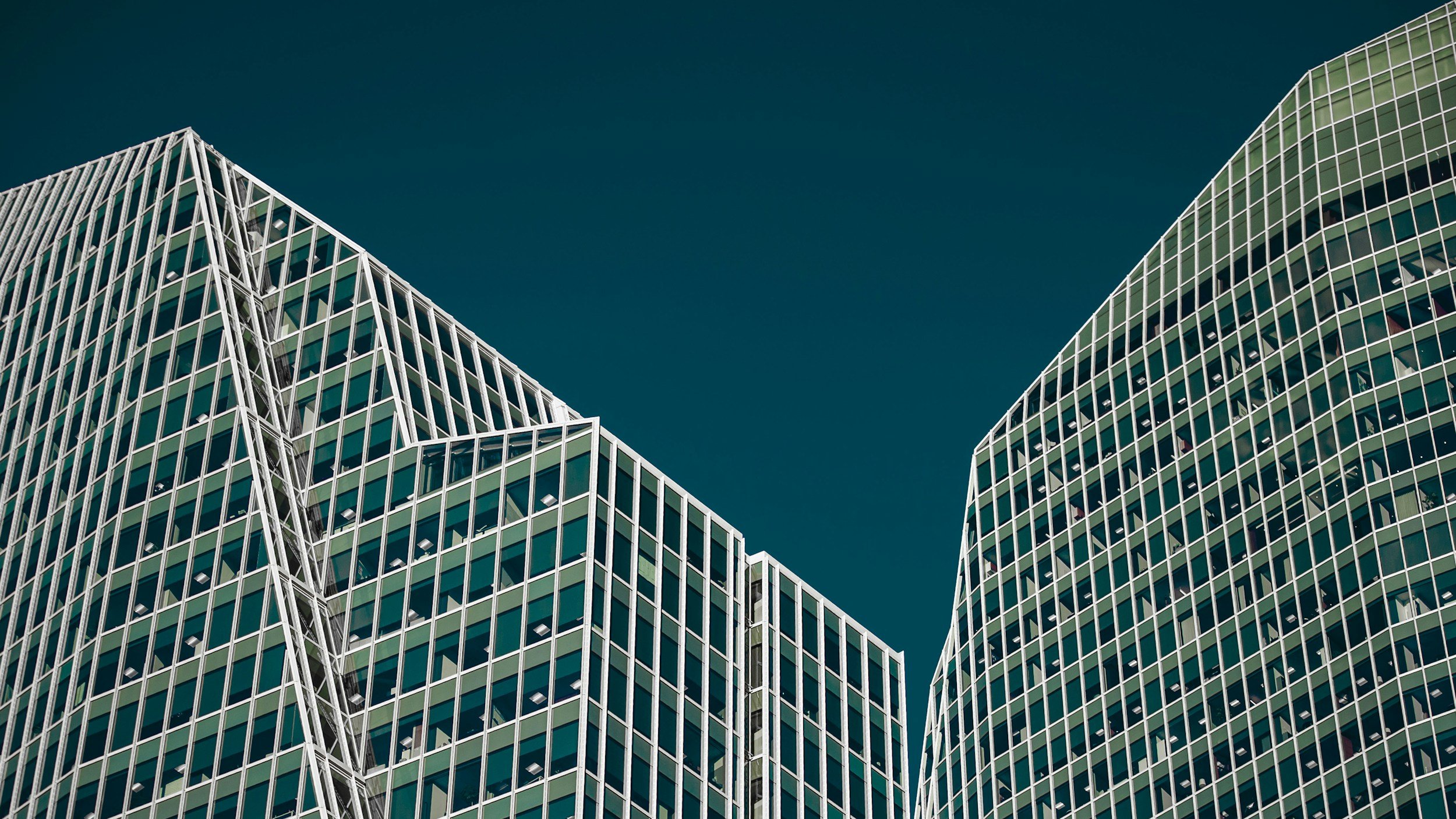 Modern glass office buildings with extensive window grid patterns against a clear blue sky.