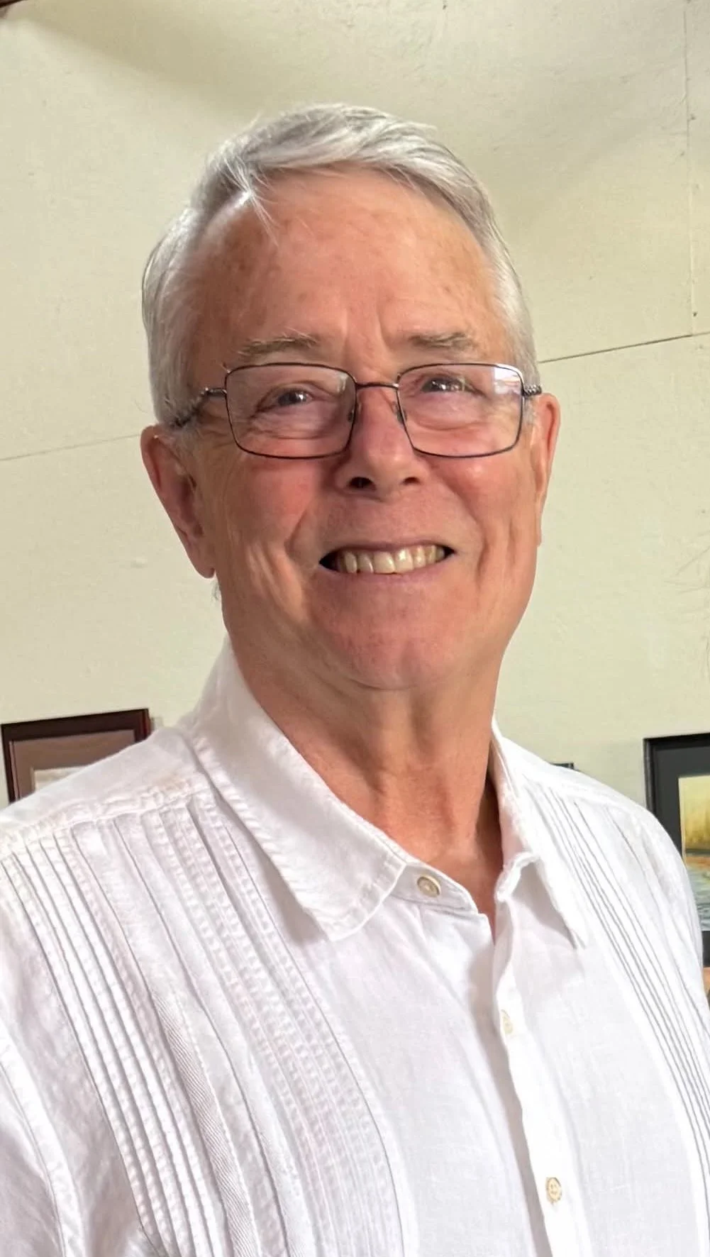 A smiling middle-aged man with gray hair, glasses, wearing a white dress shirt.