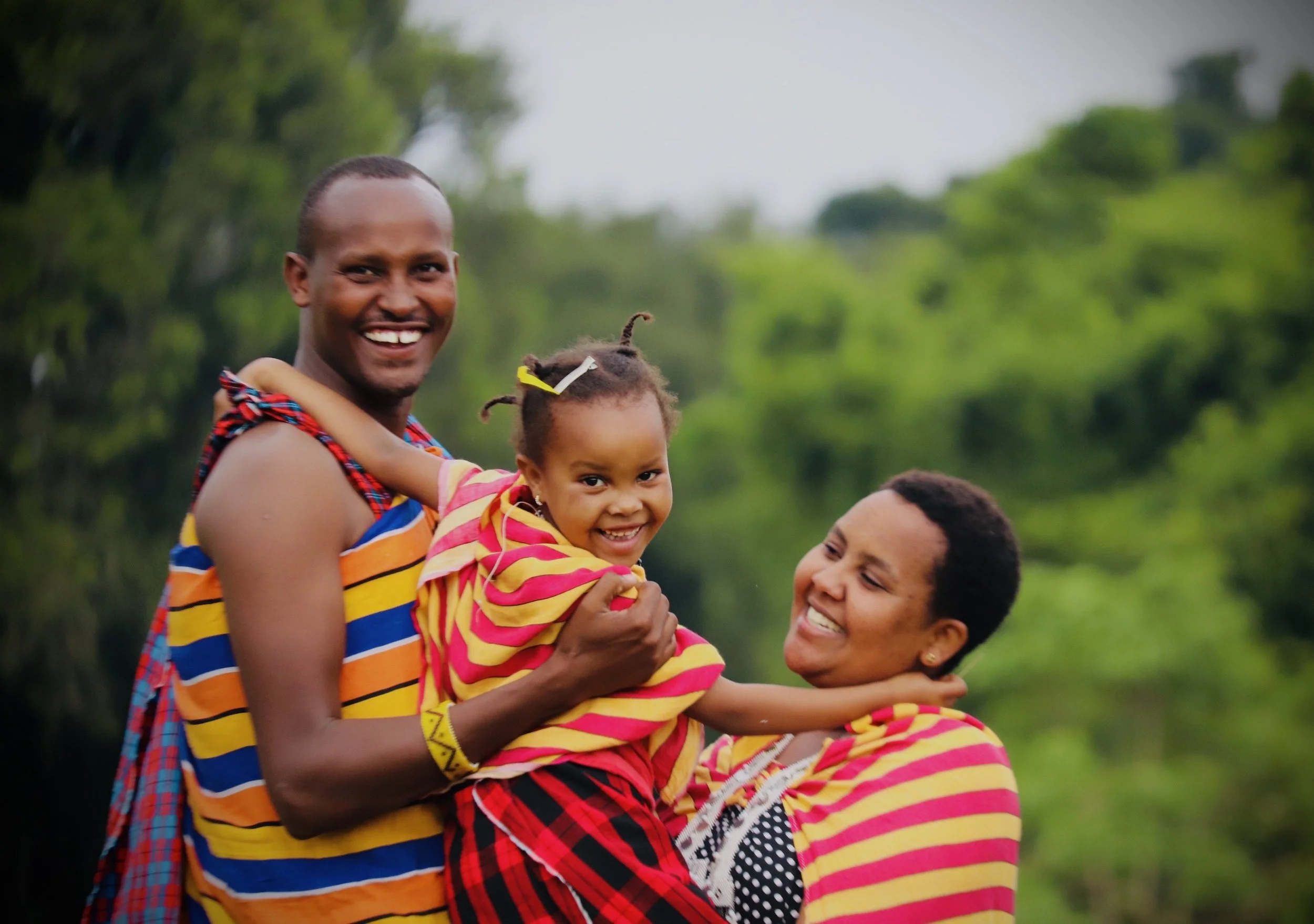 Shengana and his family smiling together outdoors.