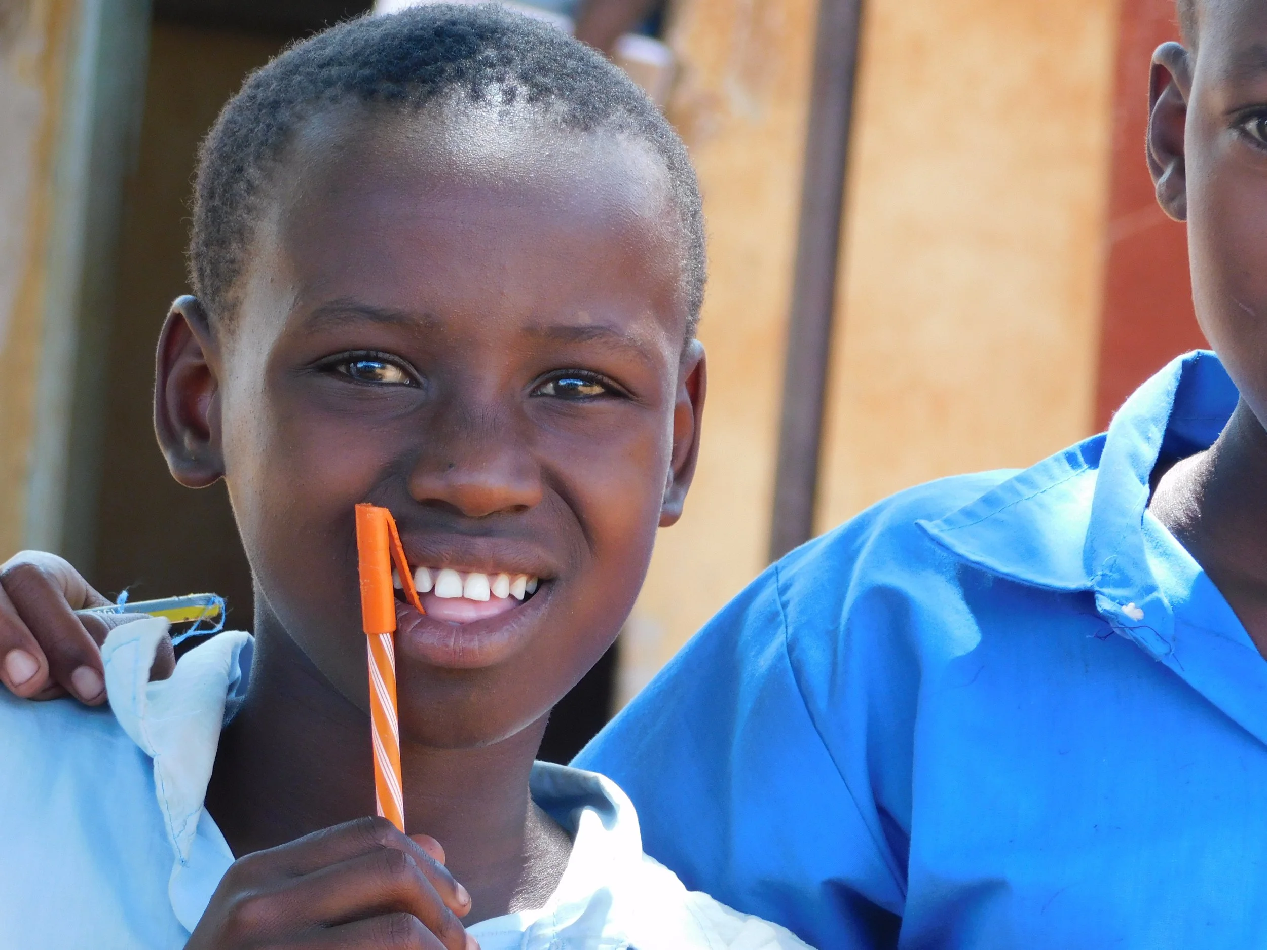 A smiling student in a blue school uniform holding a pencil.