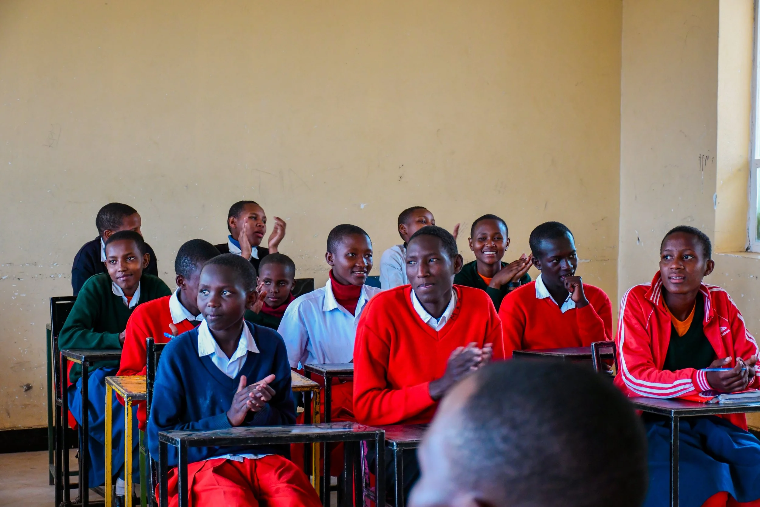 Students seated at classroom desks, some smiling and clapping.