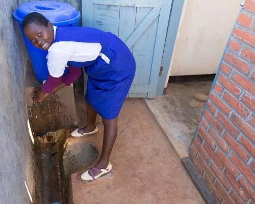 A young girl in a school uniform cleaning a water leak or stain on the ground near a wall indoors.