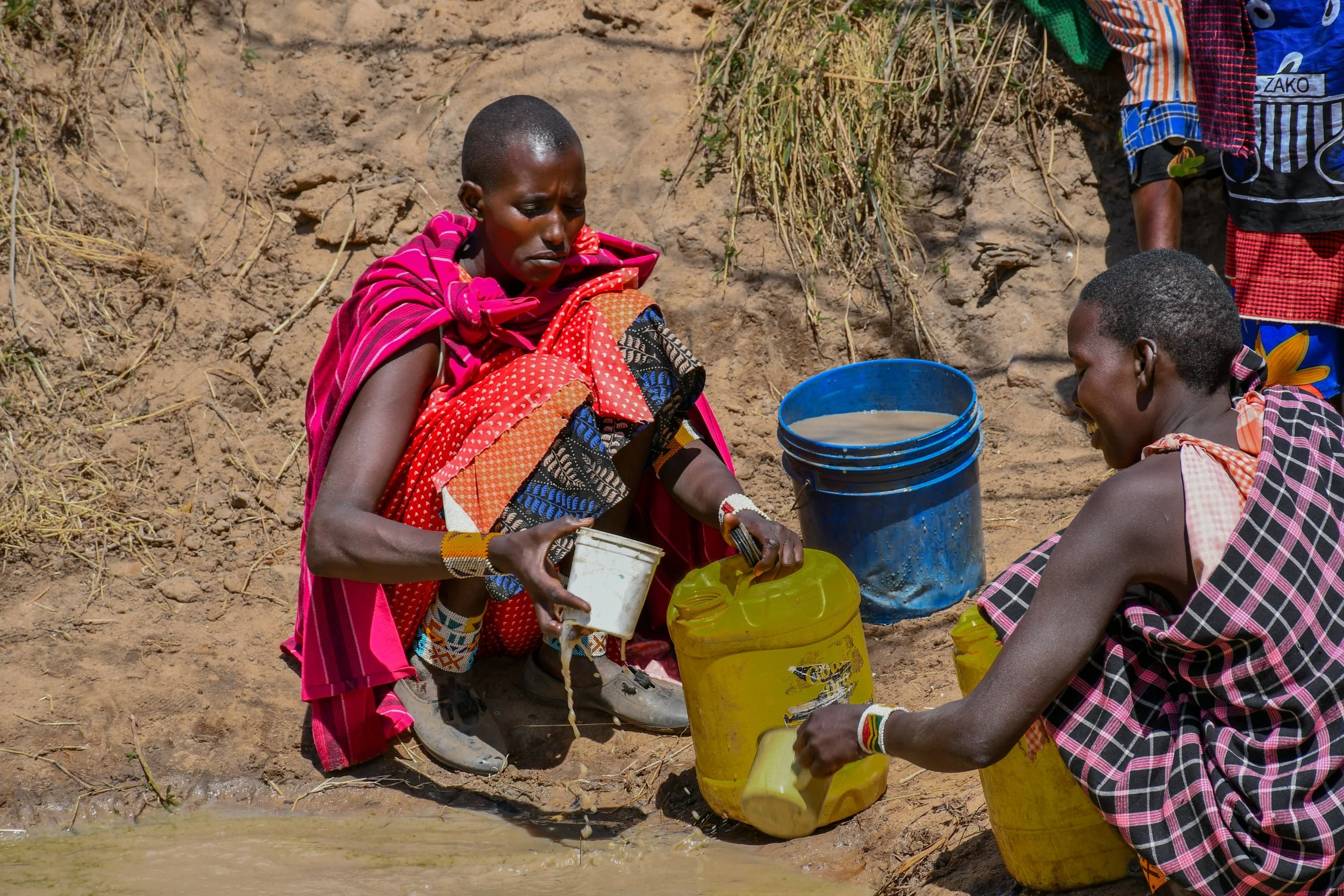 Community members filling water containers outdoors in Tanzania.