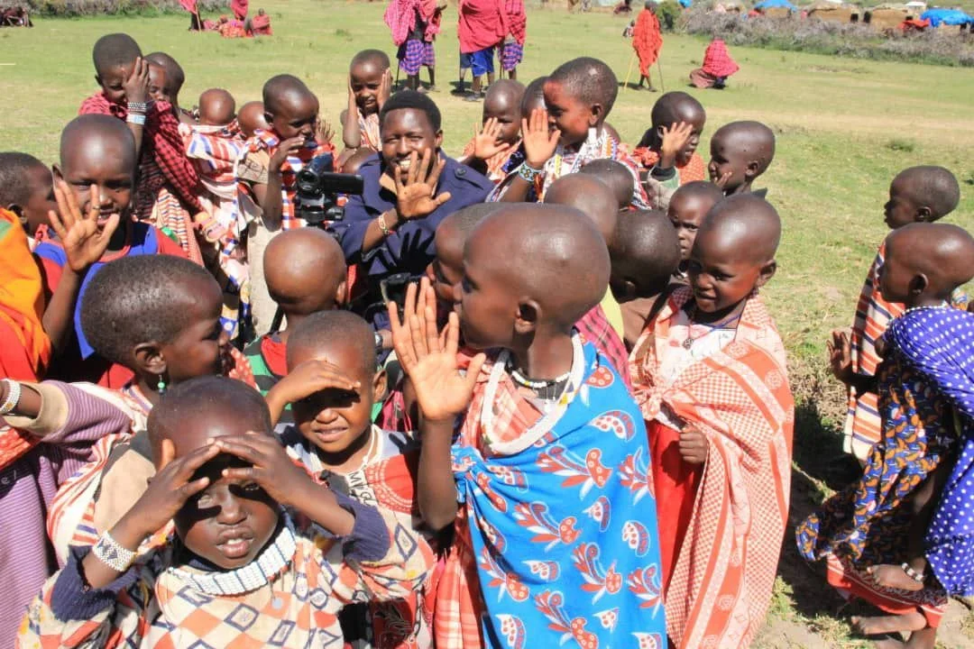 Community members and children gathered outdoors, smiling and waving.