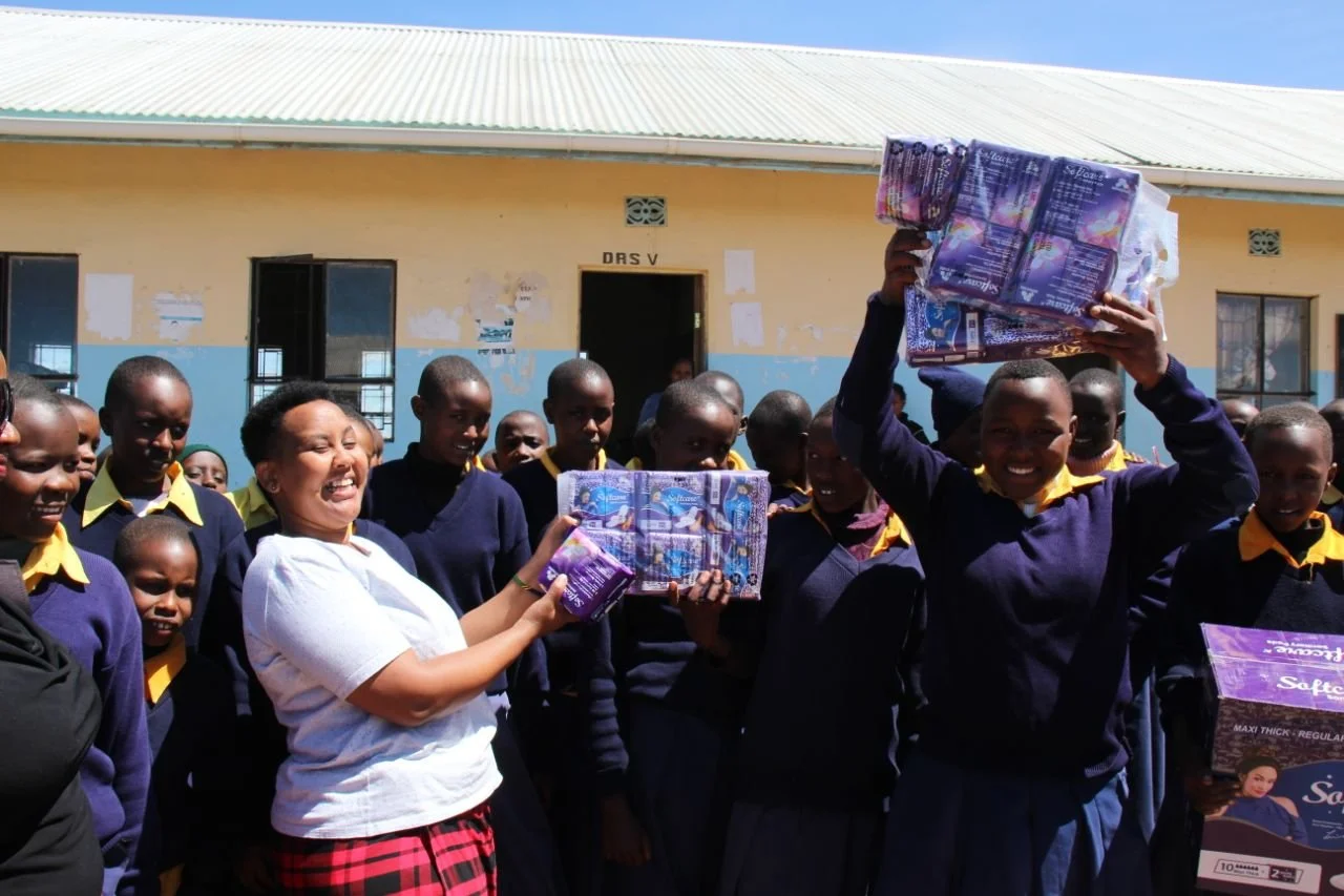 Students and an adult holding packages of sanitary pads outside a school.