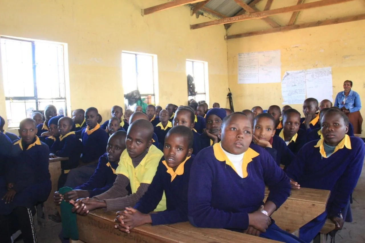 Students seated at desks in a classroom wearing navy and yellow uniforms.
