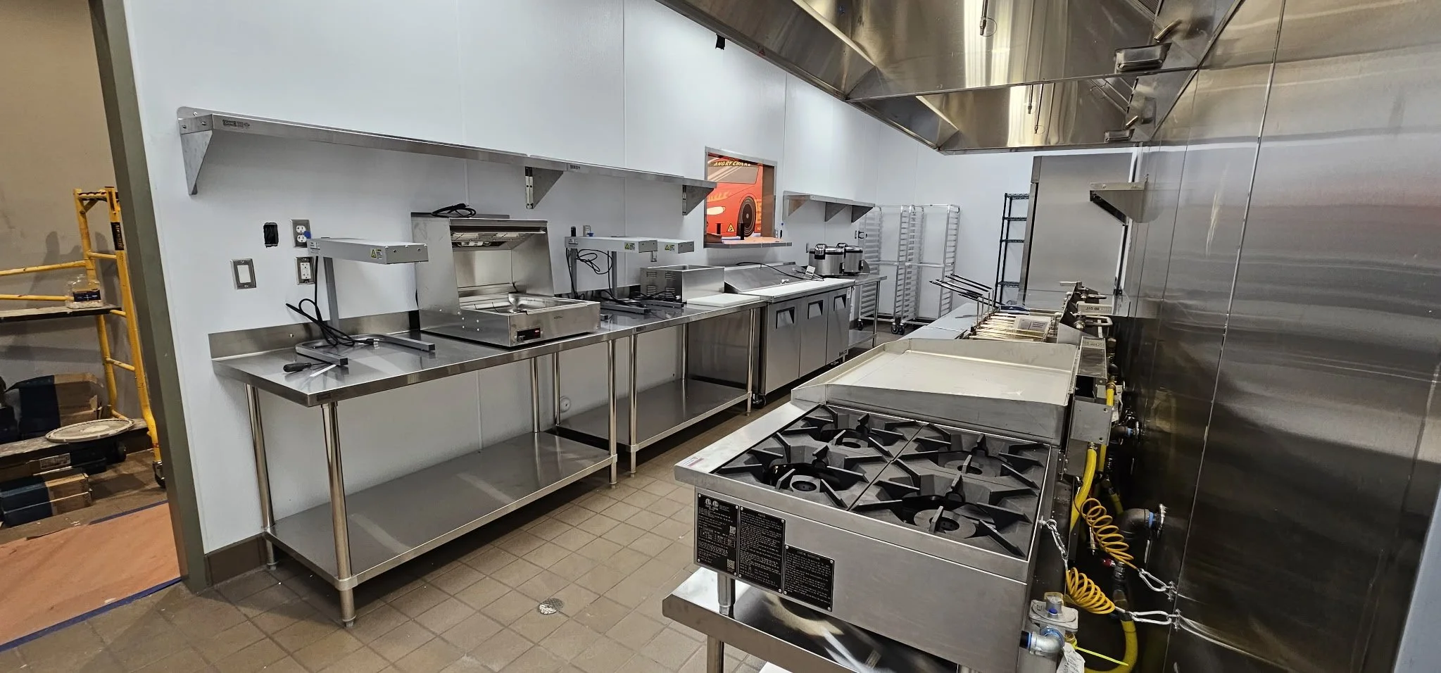 Commercial kitchen with stainless steel appliances, gas stove, counters, and shelves.