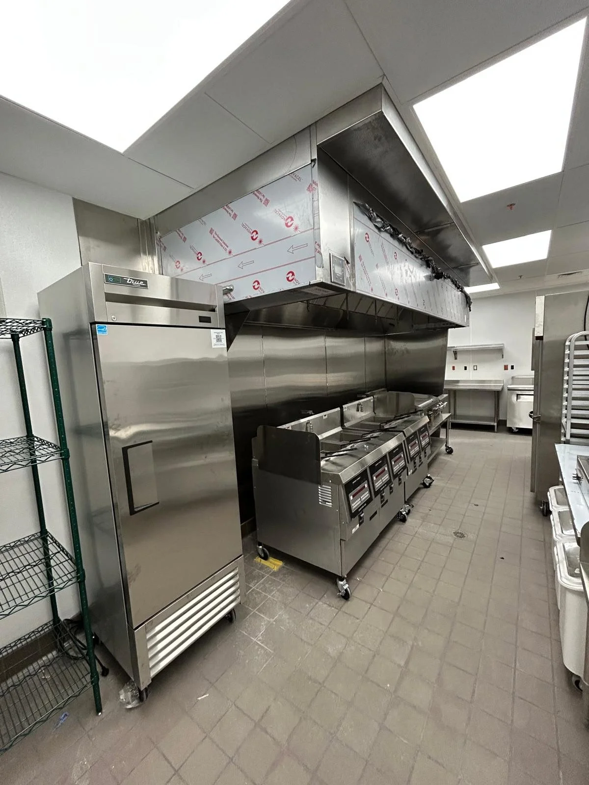 Commercial kitchen with stainless steel appliances, including an oven, stovetop, and exhaust hood.