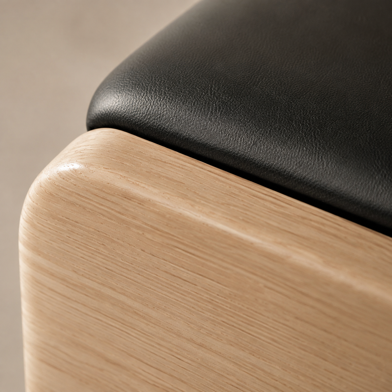 Detalle de una pieza de mobiliario con acabado en madera clara y cojín negro en la parte superior.