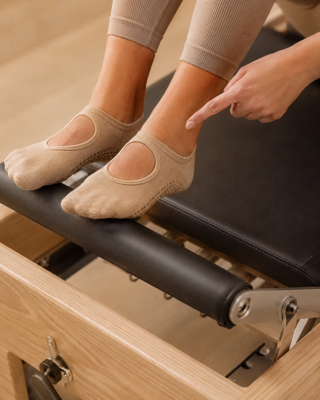 Persona con calcetas beige sentada en Reformer, tocando su tobillo izquierdo.