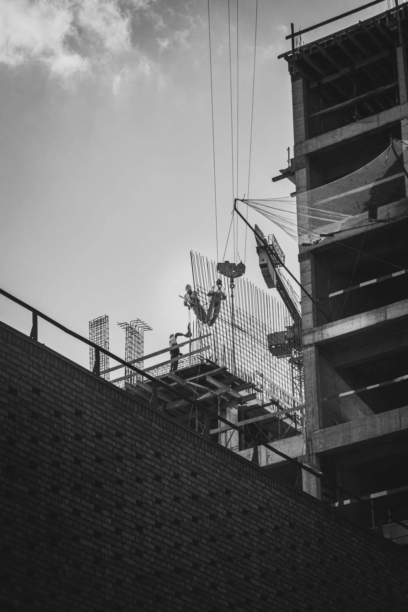 Black and white photo of construction workers at a building site, working on the upper floors of a partially constructed multi-story building with scaffolding.