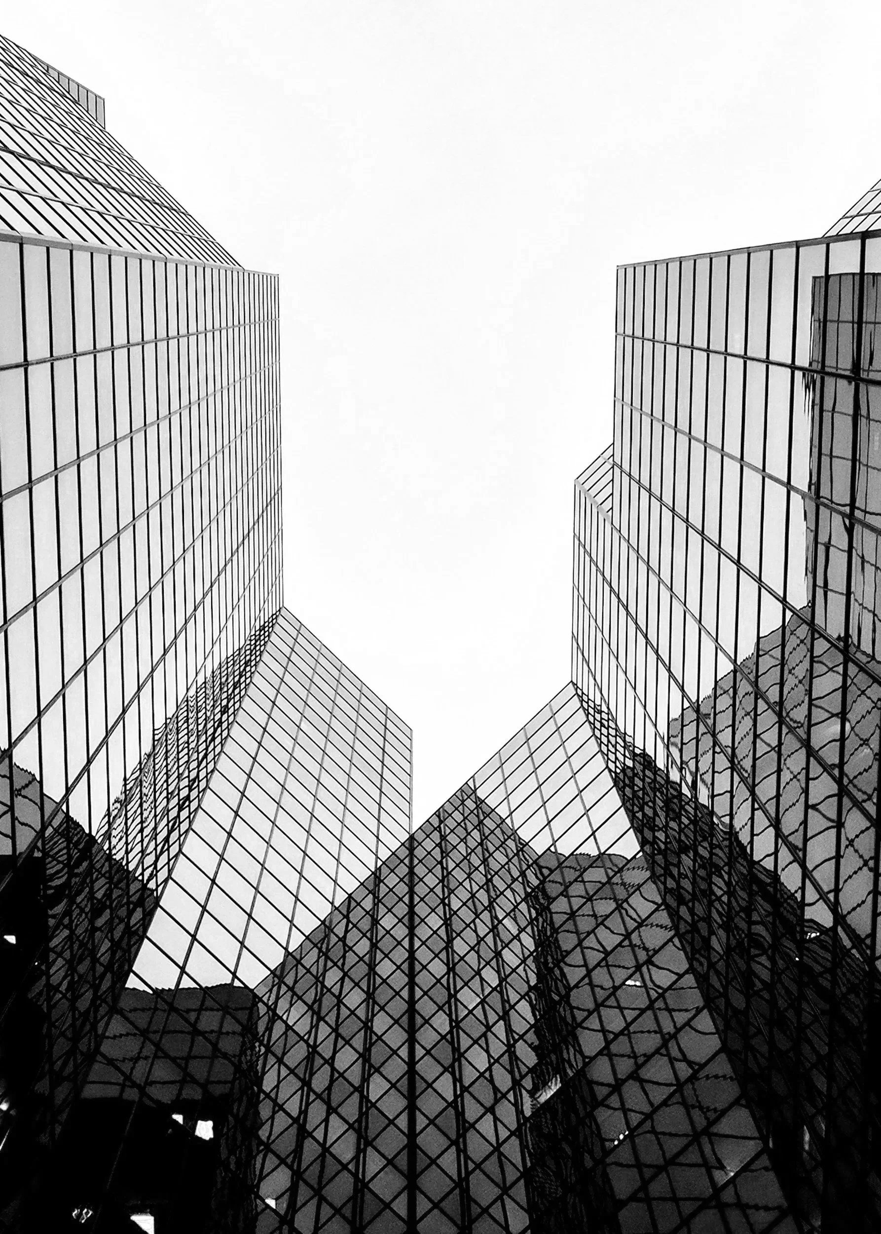 Two tall modern glass office buildings seen from below, looking up at the overcast sky.
