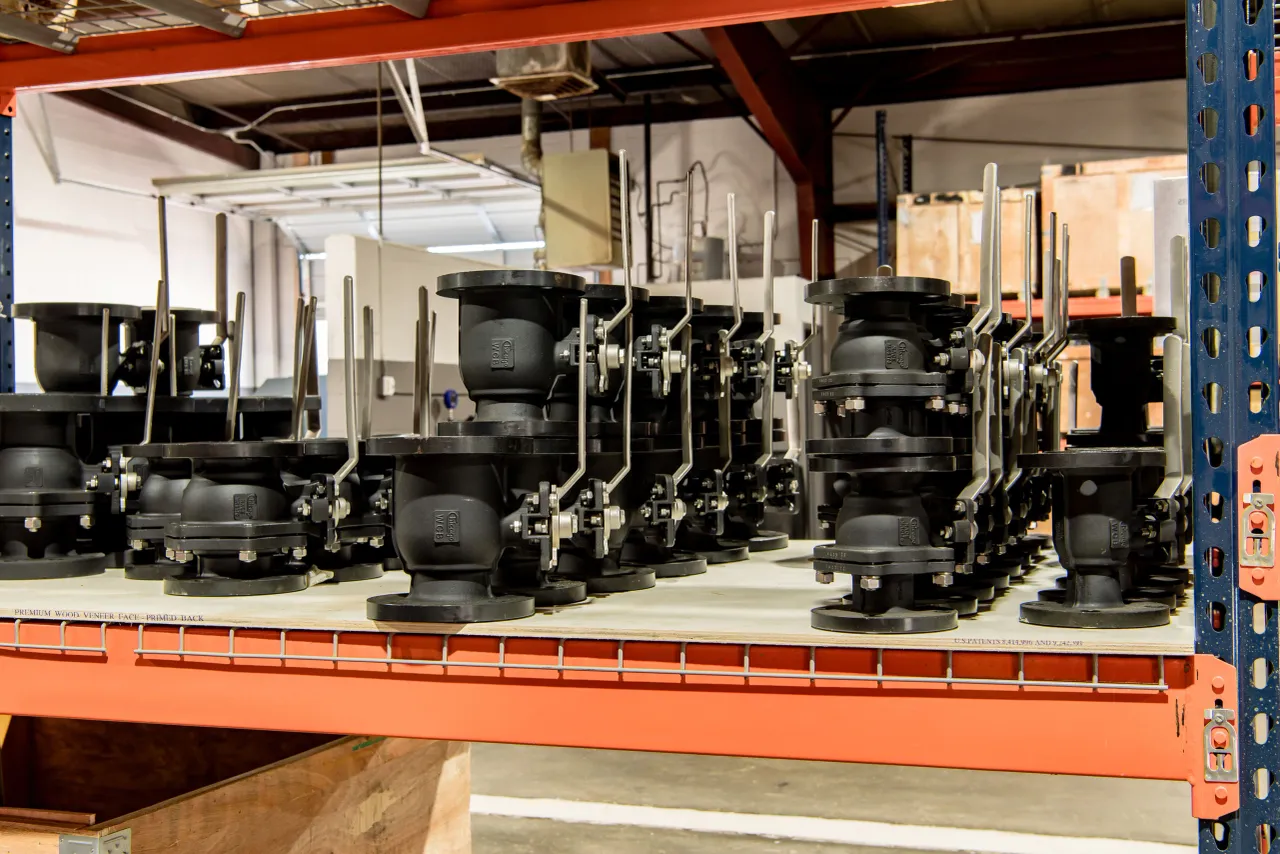 Multiple black industrial valves with metal handles on a warehouse shelf.