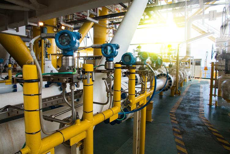Industrial pipes and valves in a factory with sunlight shining through windows.