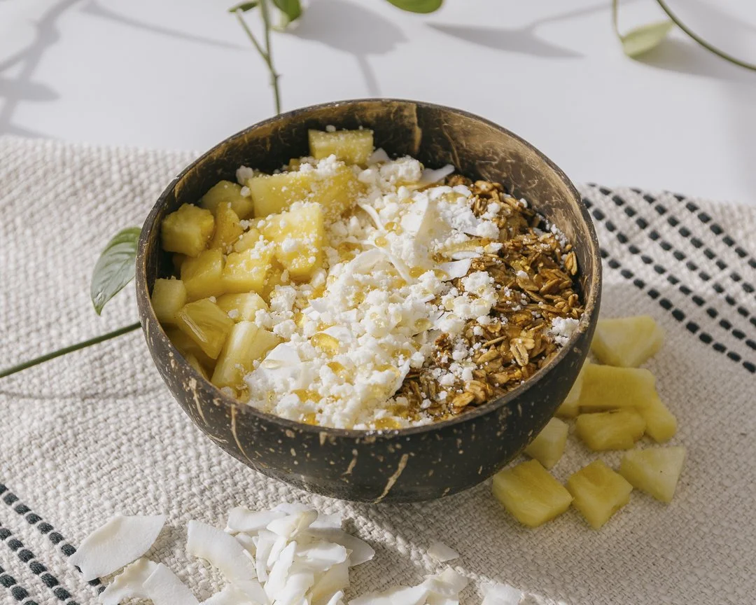 A bowl of chopped pineapple with coconut flakes and granola on top, placed on a woven cloth with some pineapple pieces and coconut flakes nearby for Innerlight Juice.