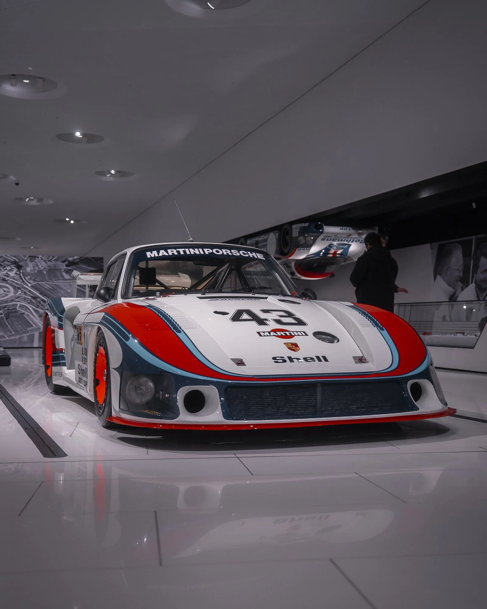 A race car with Martini racing colors and sponsorship logos on display, likely at a museum or auto show.