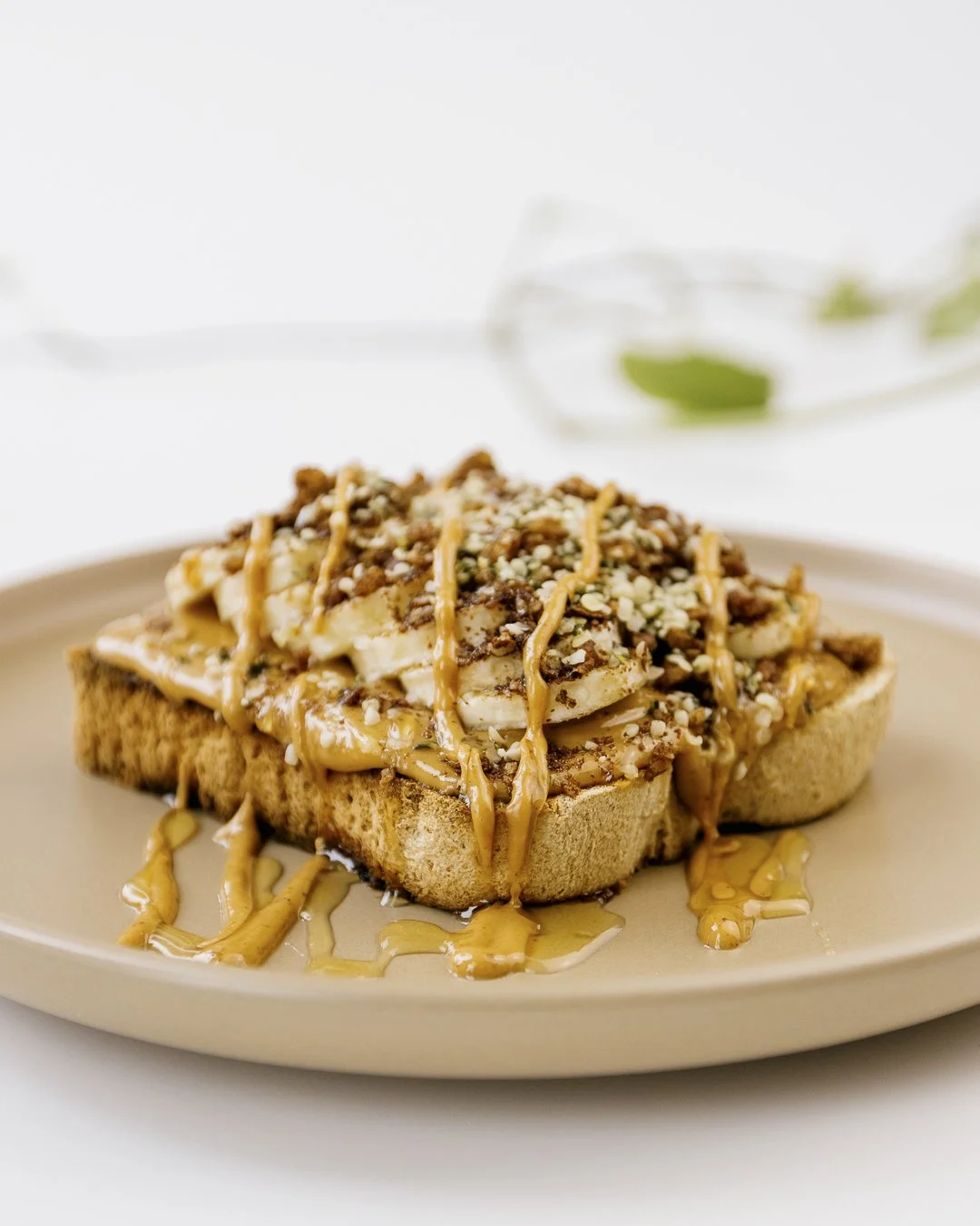 A piece of toasted bread topped with banana slices, chopped nuts, and caramel drizzle, served on a beige plate.