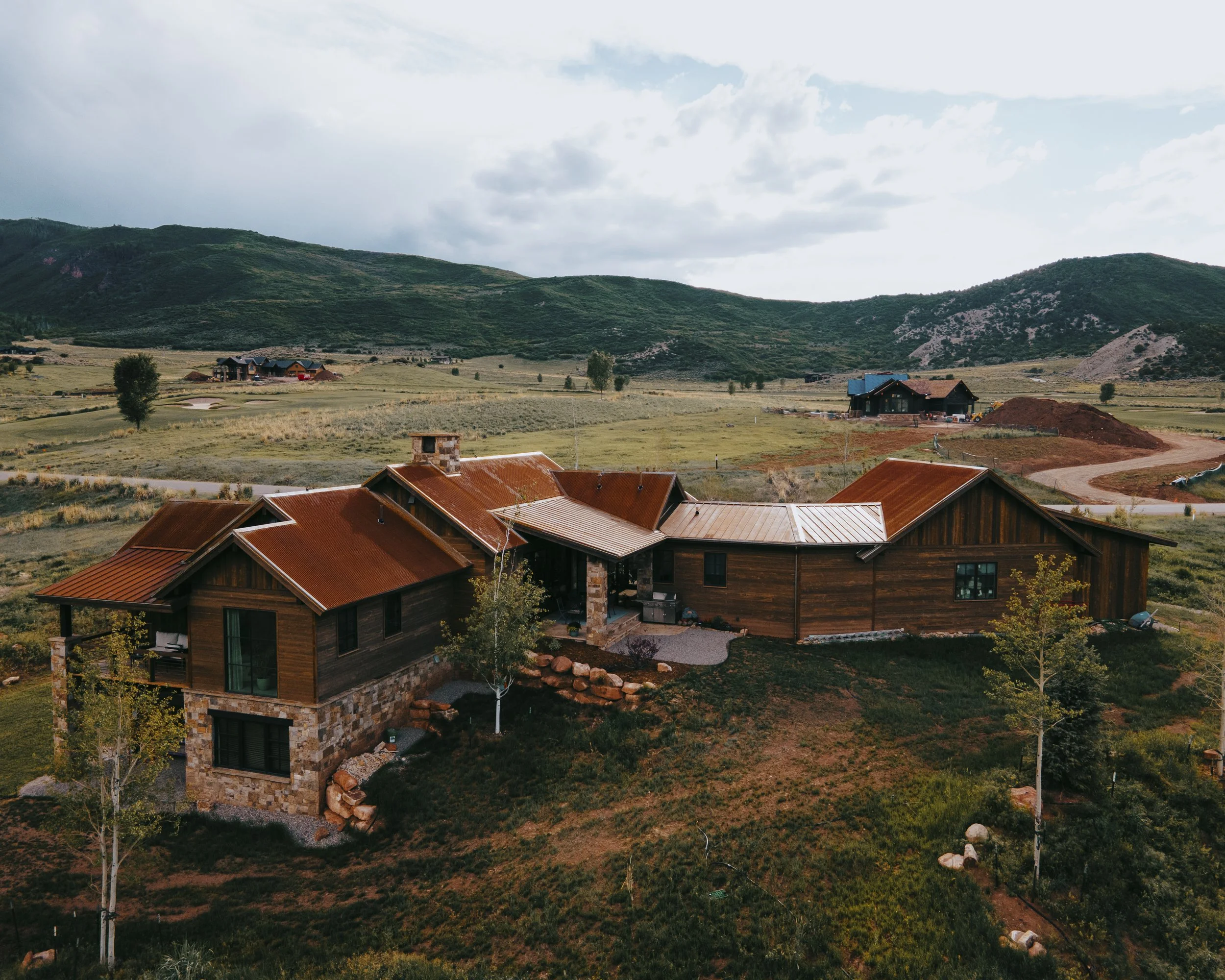 A scenic view of a mountainous landscape with houses, green hills, and a partly cloudy sky, capturing roofing services with a Drone