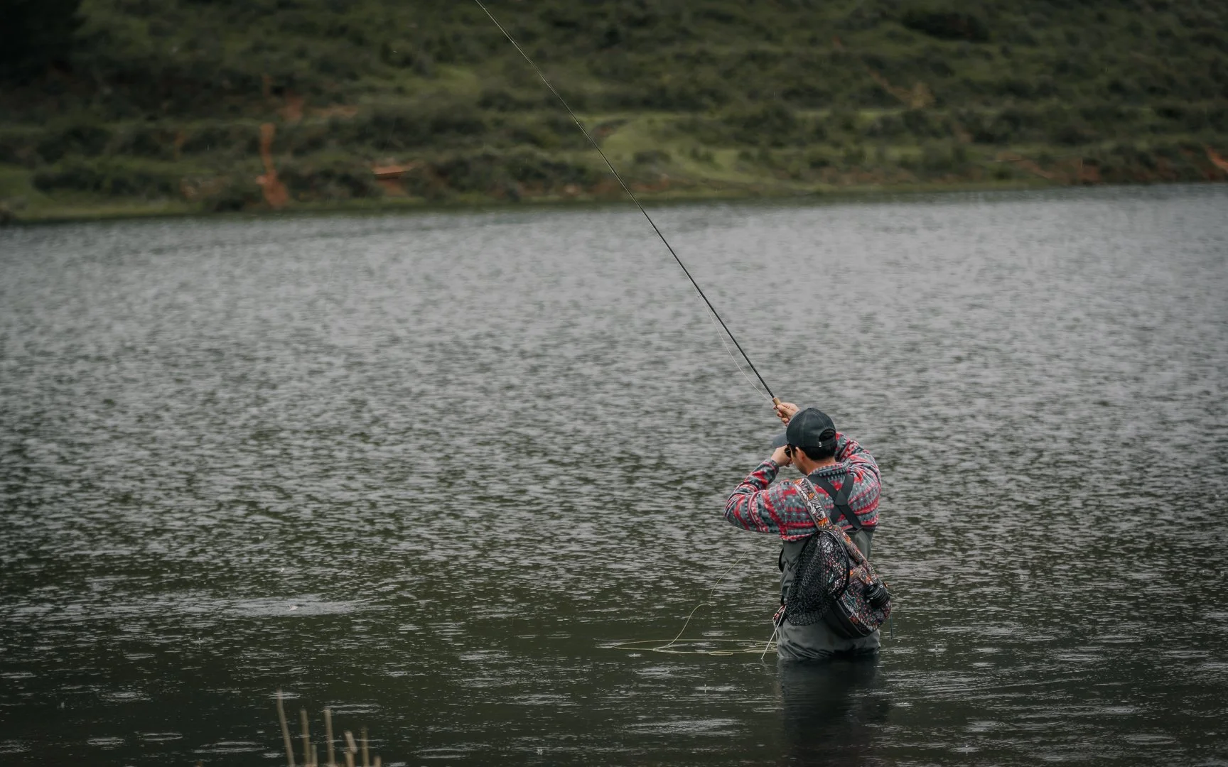 Person fishing in a lake with hilly landscape in the background.