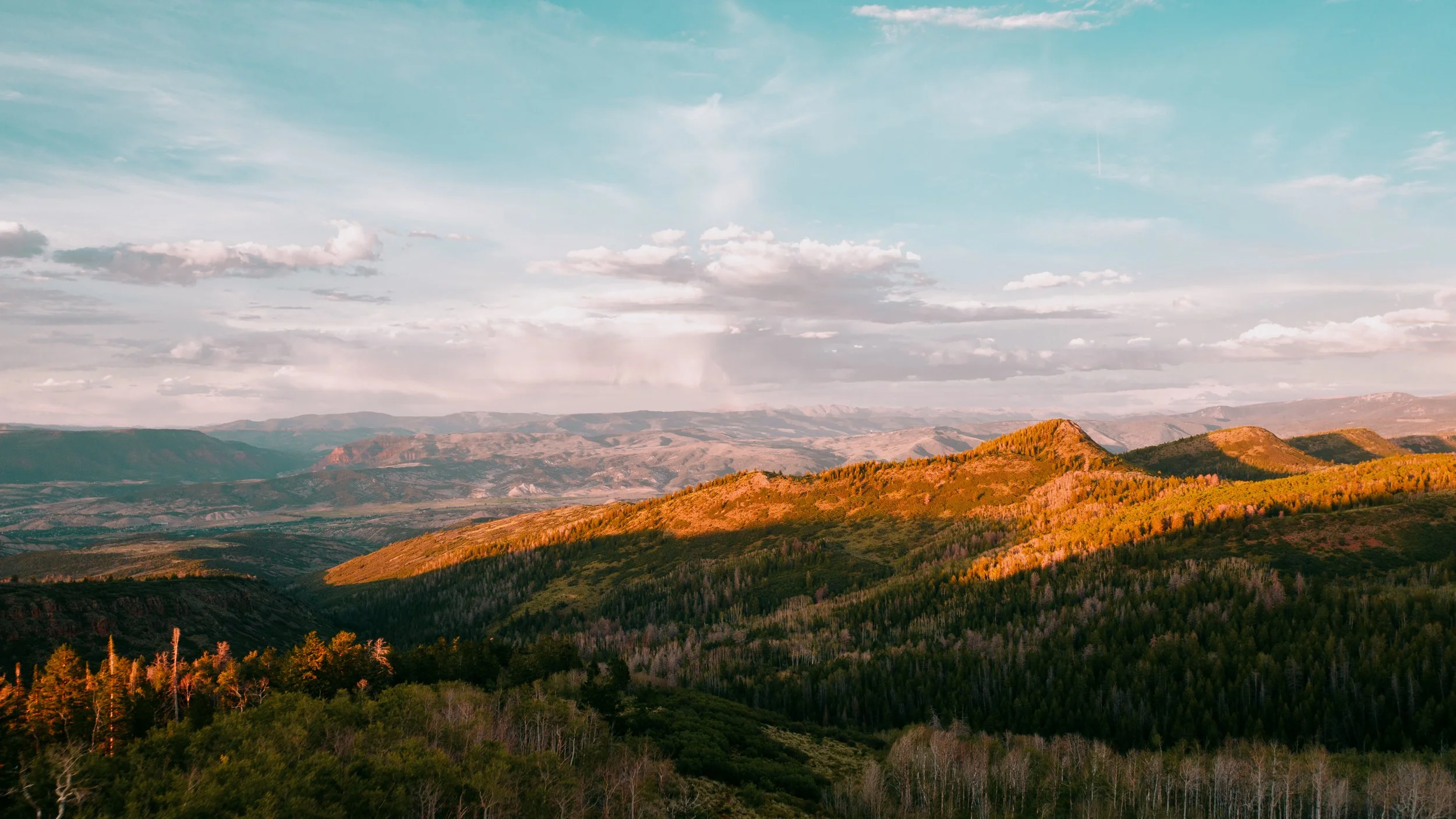 Scenic view of rolling hills and mountains with a partly cloudy sky during sunset.