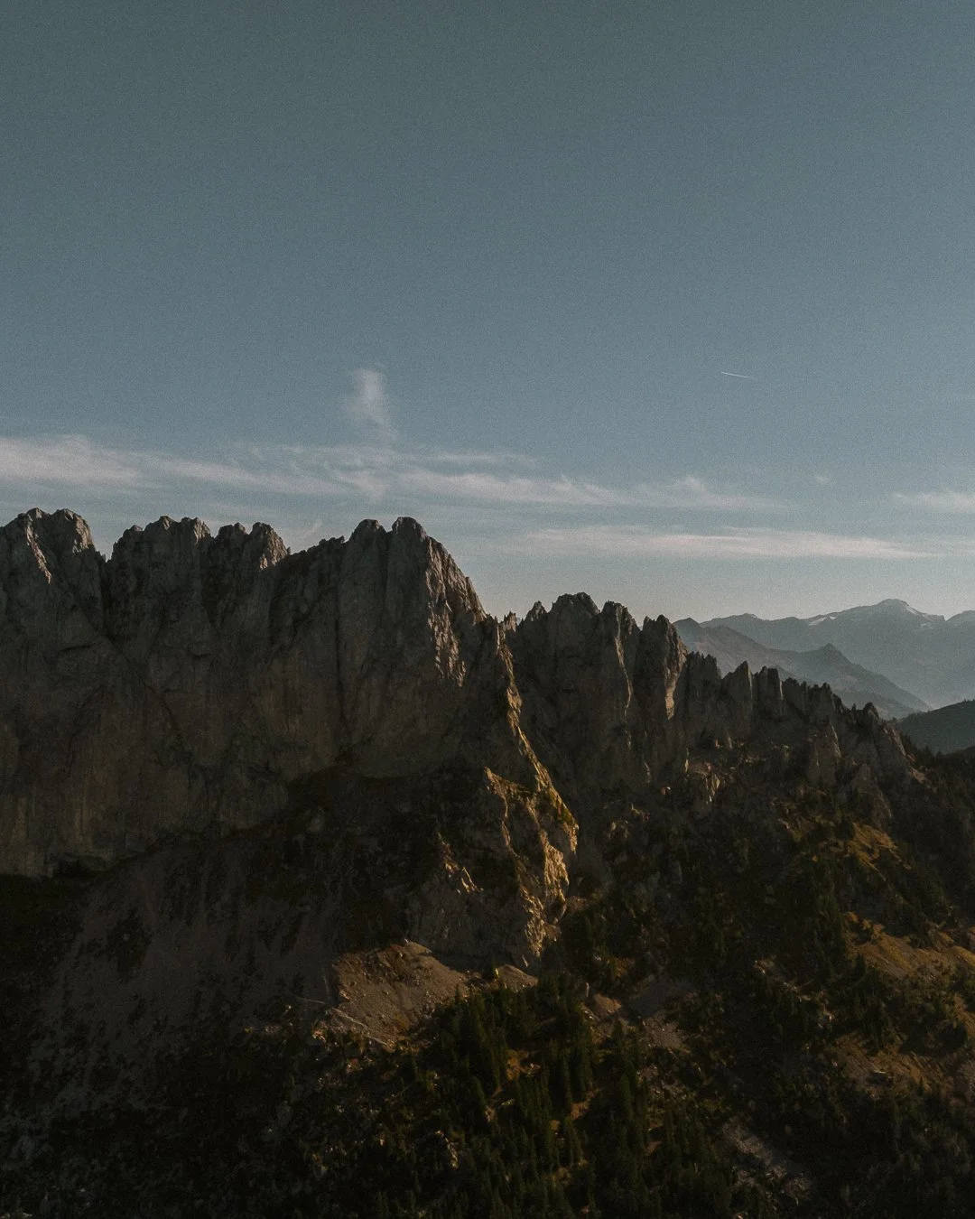 A mountain range with rugged peaks and a clear sky above, possibly during sunrise or sunset.