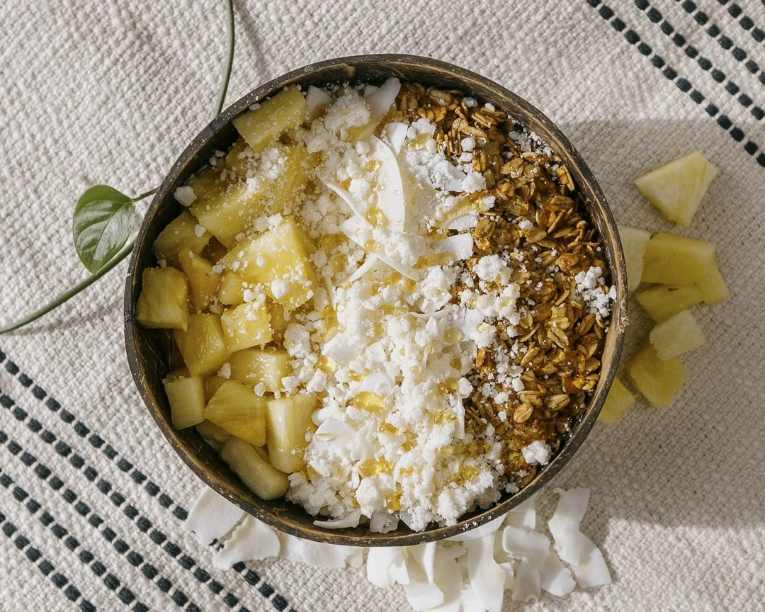 A bowl containing diced pineapple, coconut flakes, granola, and shredded coconut squares on a textured cloth background for Innerlight Juice.