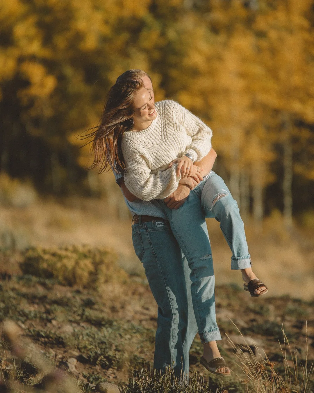 A woman is being lifted in a field during autumn with trees in the background.