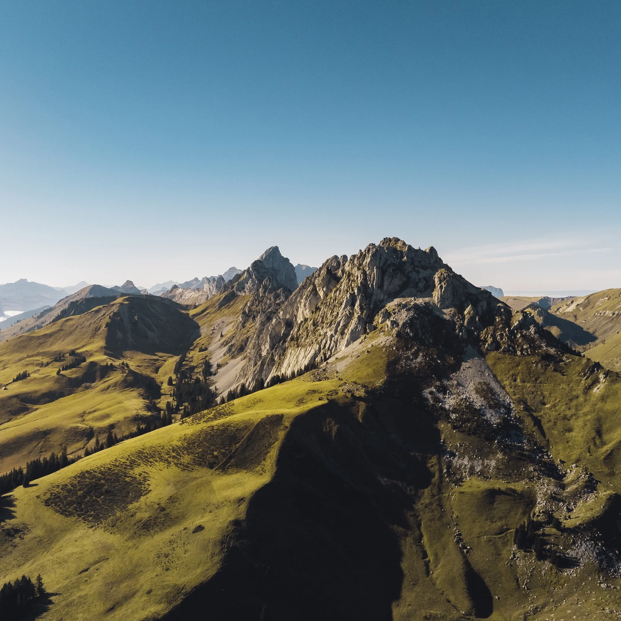 Scenic mountain landscape with rugged peaks, rolling green hills, and a clear blue sky in the Swiss Alps