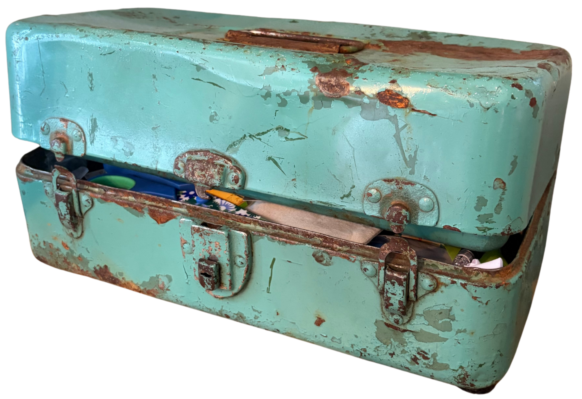 Close-up of a rusty, old, green metal toolbox with peeling paint and visible rust spots, containing children’s scissors and other items.