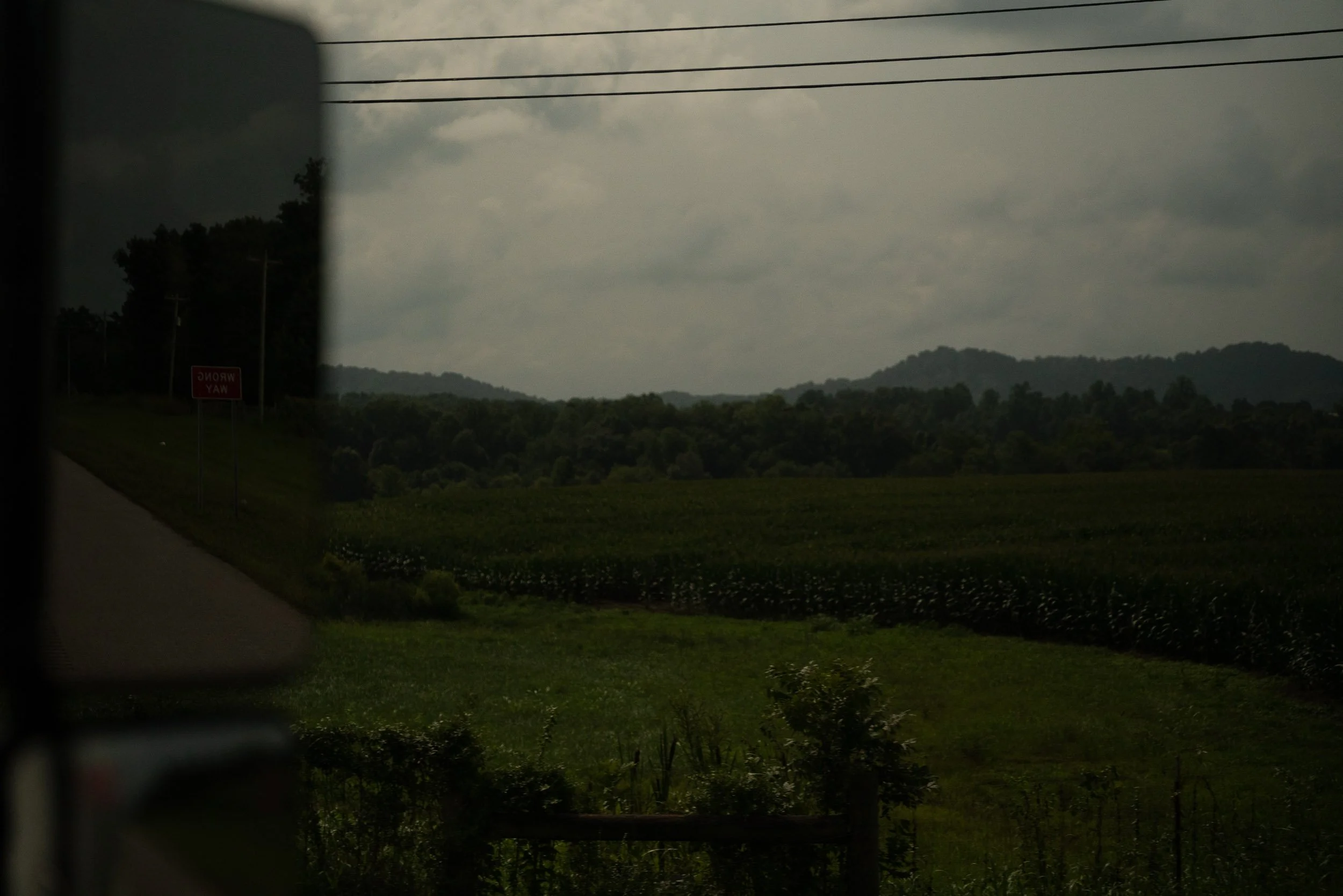 Landscape view of distant mountains and a cloudy sky, seen through a vehicle window with a reflection and some interior elements visible.