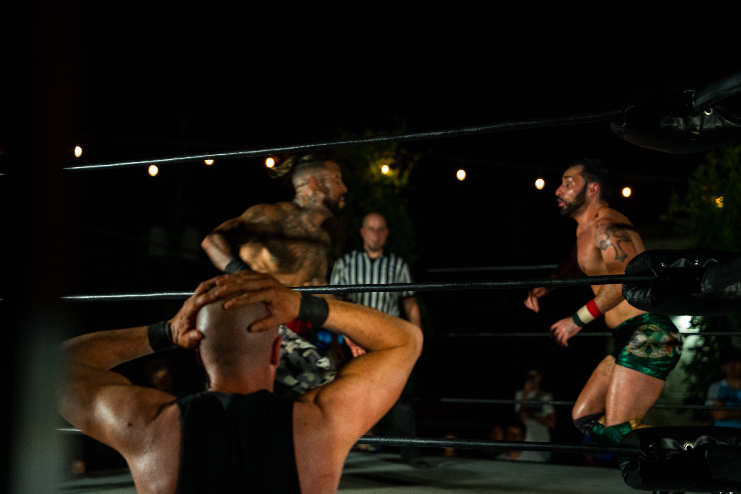 Boxers in a ring during a match, with one referee visible in the background under string lights at night.