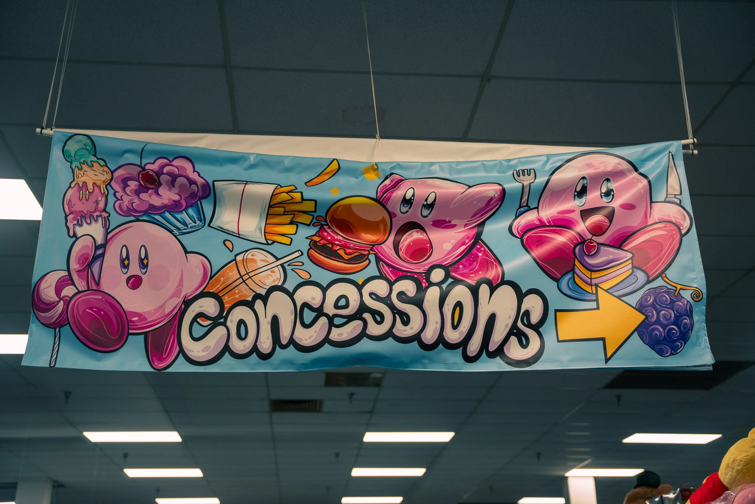 Colorful banner with cartoon cookies and food items, including an ice cream cone, cupcake, burger, and cake, with playful eyes and smiling faces, advertising a concession stand or similar event.