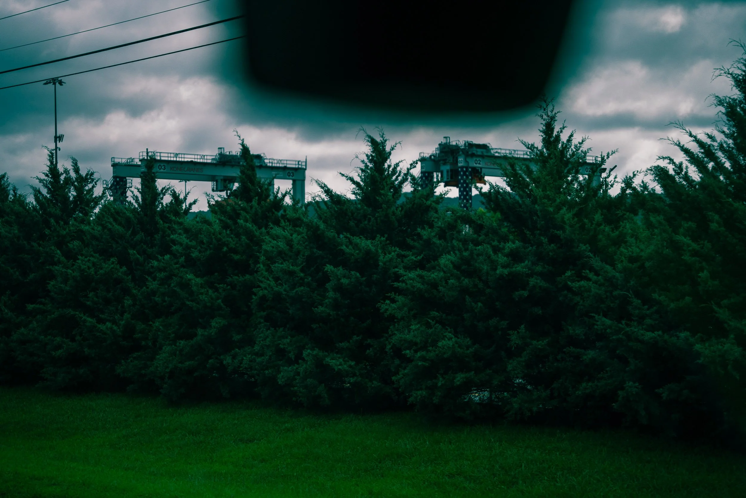 Overcast sky with dark clouds over a landscape of trees, power lines, and a metal structure.
