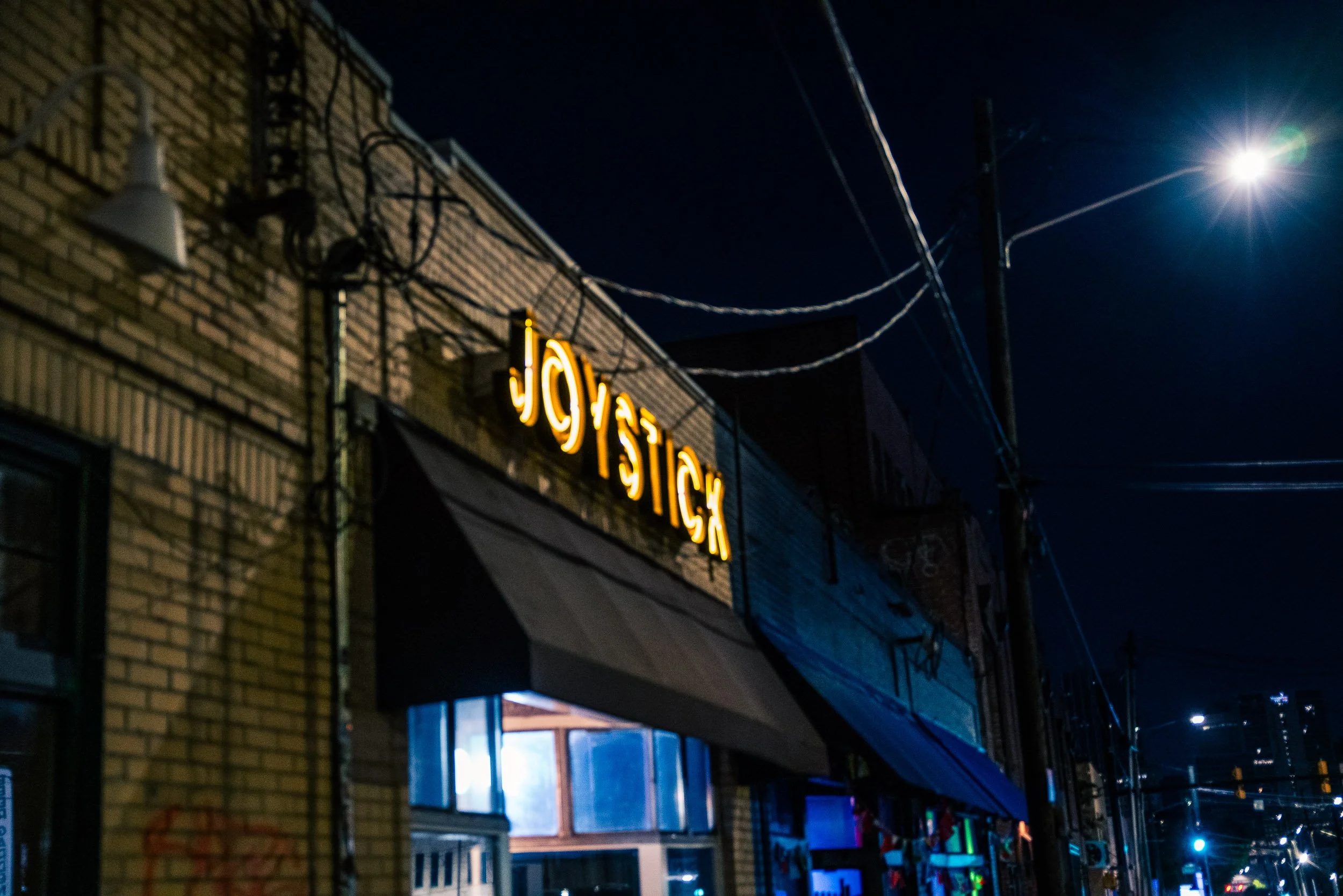 Nighttime street scene with a brick building, illuminated sign, power lines, and a bright streetlight in the sky.