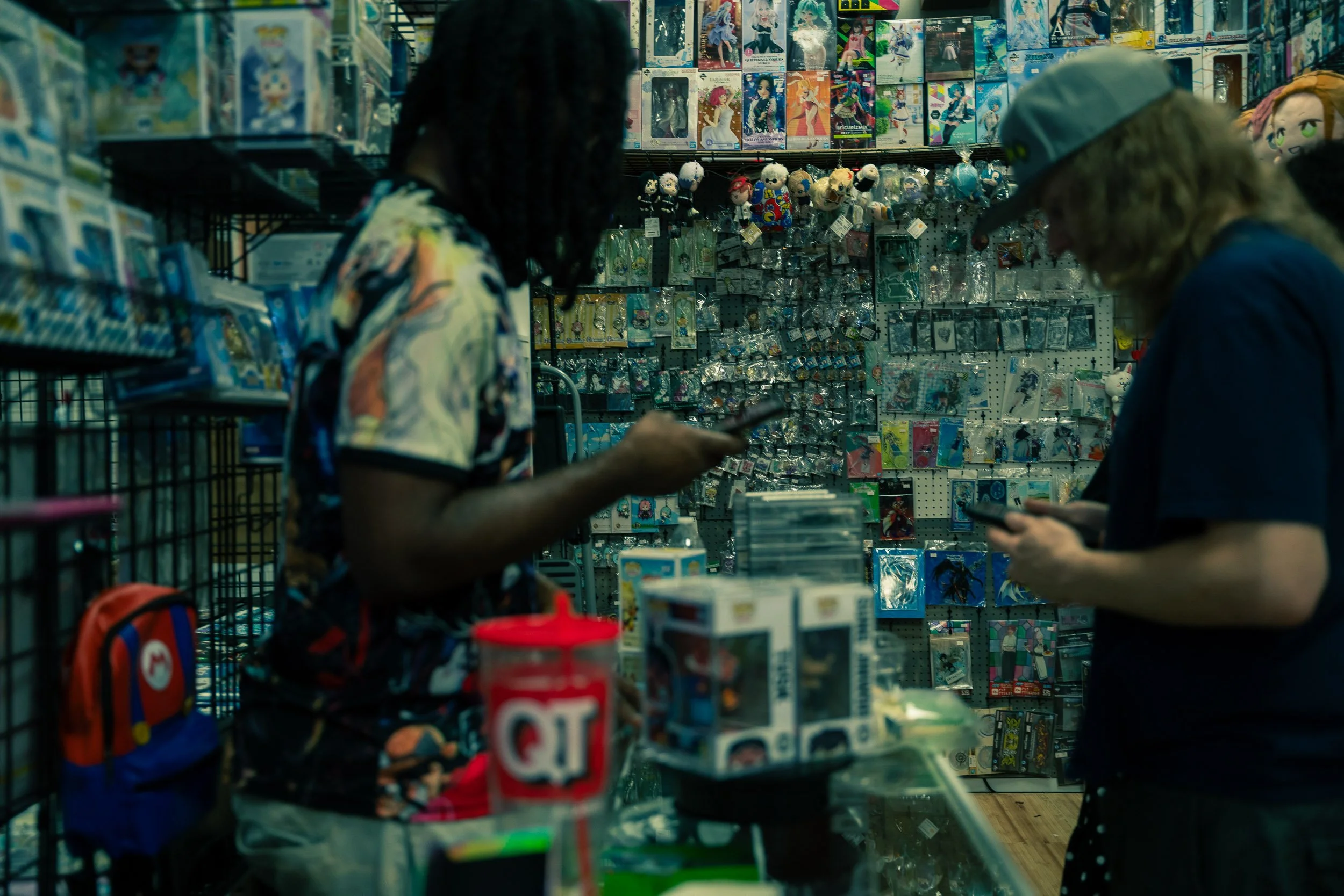 Two people shopping at a toy store, browsing shelves filled with collectibles, dolls, and merchandise.