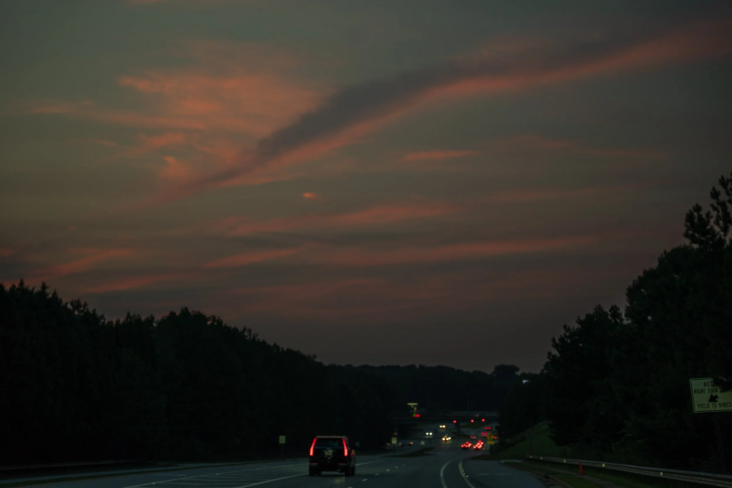 A highway at dusk with cars traveling and a colorful sunset sky with pink and orange clouds.