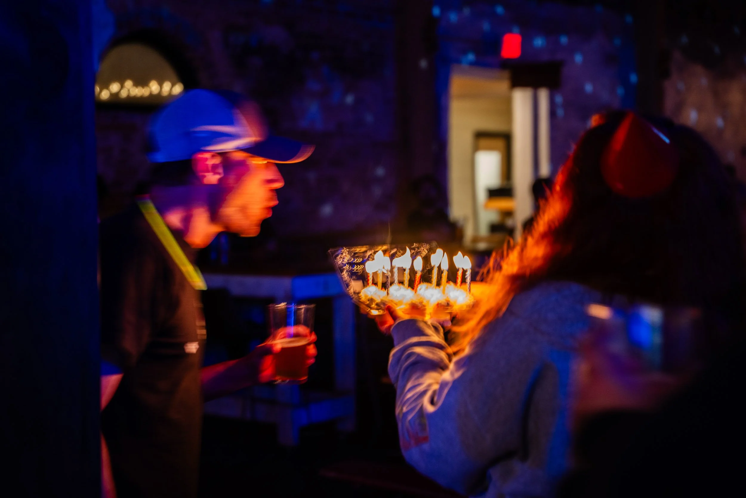 People celebrating a birthday with cake and candles in a dimly lit room.