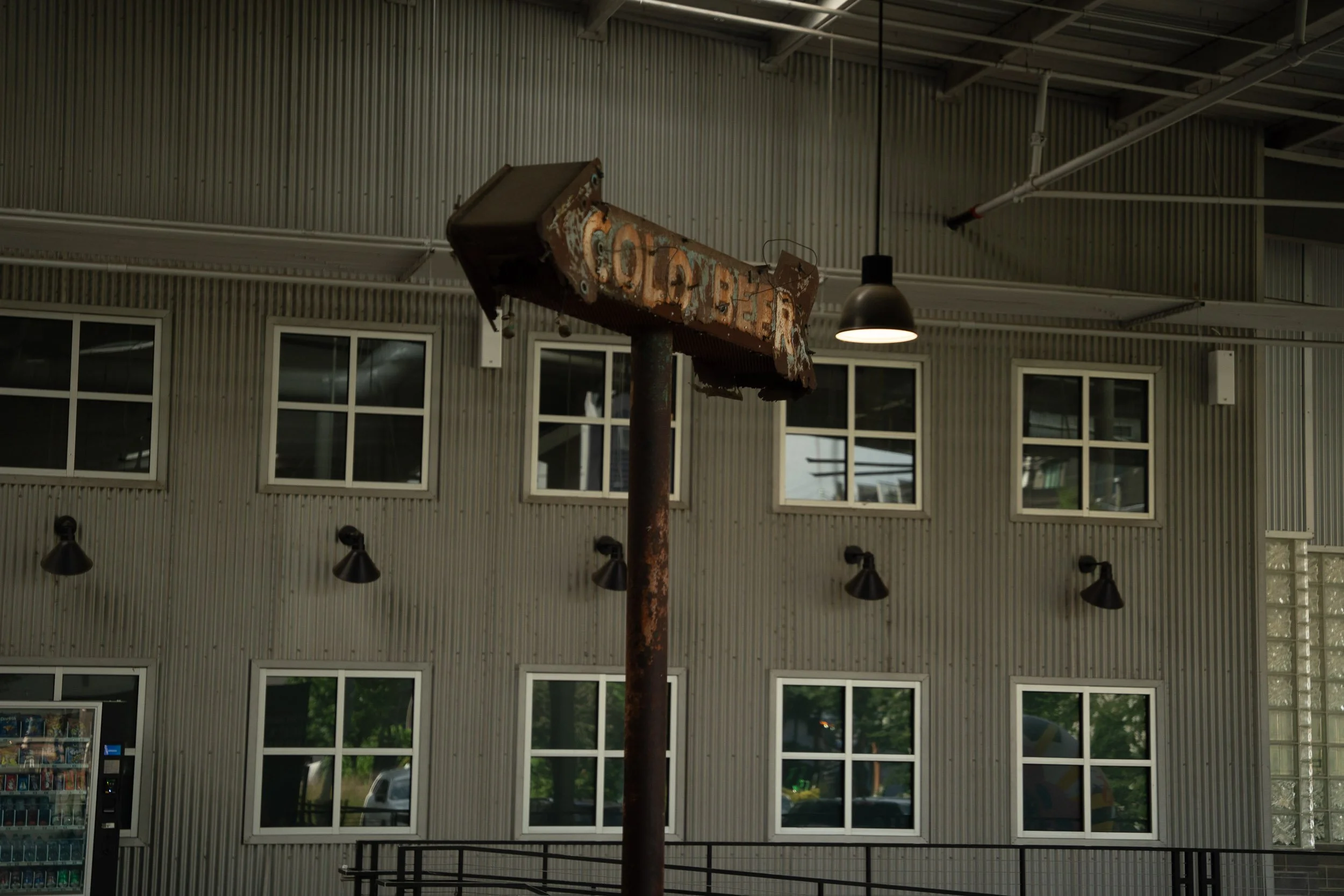Rusty, abandoned water ski tramper hanging from the ceiling inside a building with large windows and a corrugated metal ceiling.
