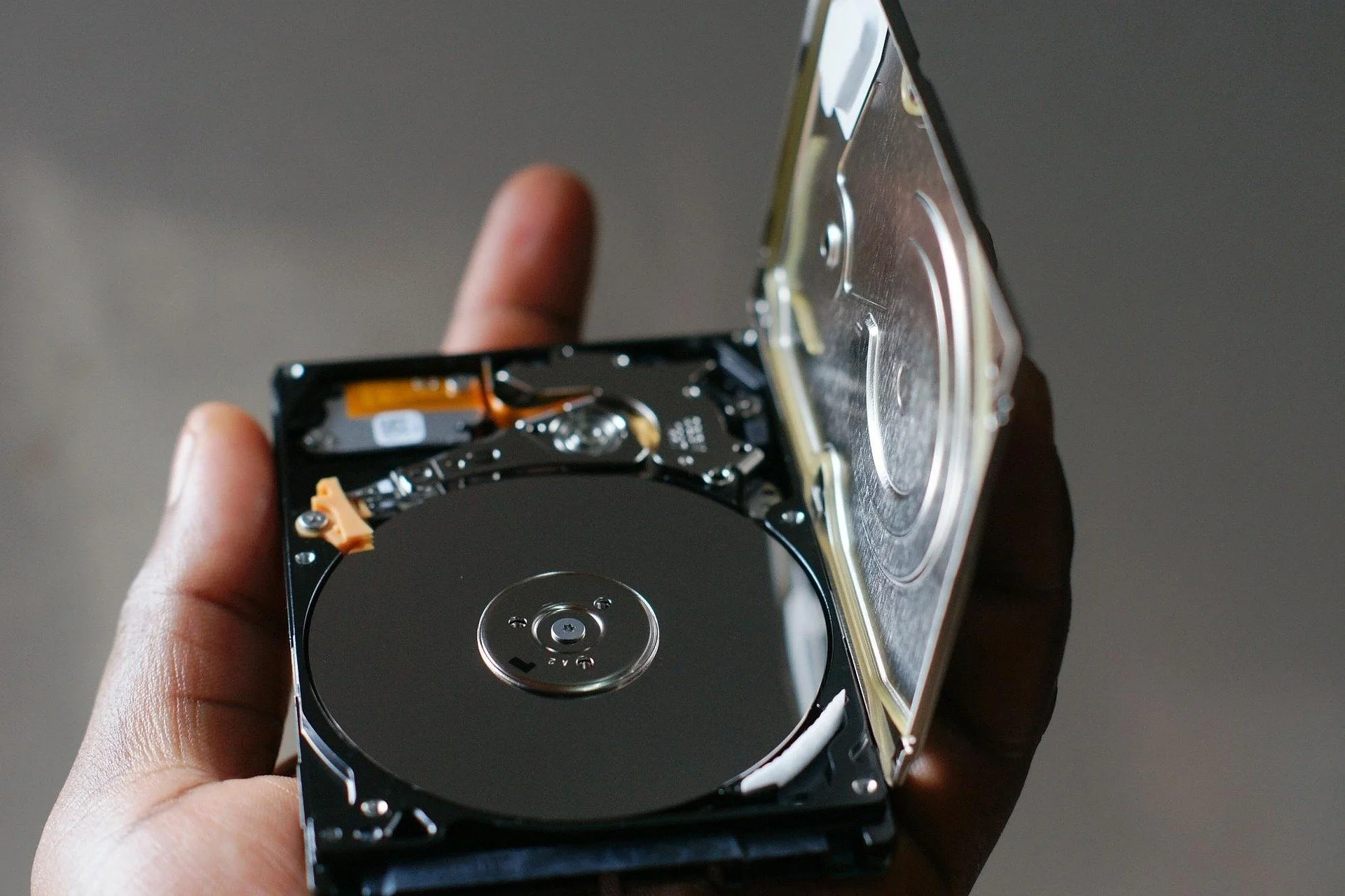 Person holding a damaged hard drive with an open casing, exposing the internal components.