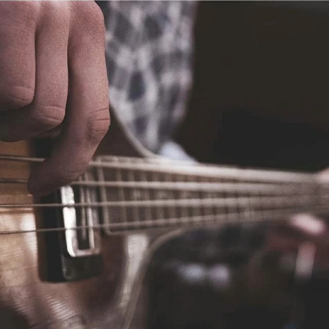 Close-up of a person playing an acoustic guitar, focusing on their fingers pressing the strings on the fretboard.