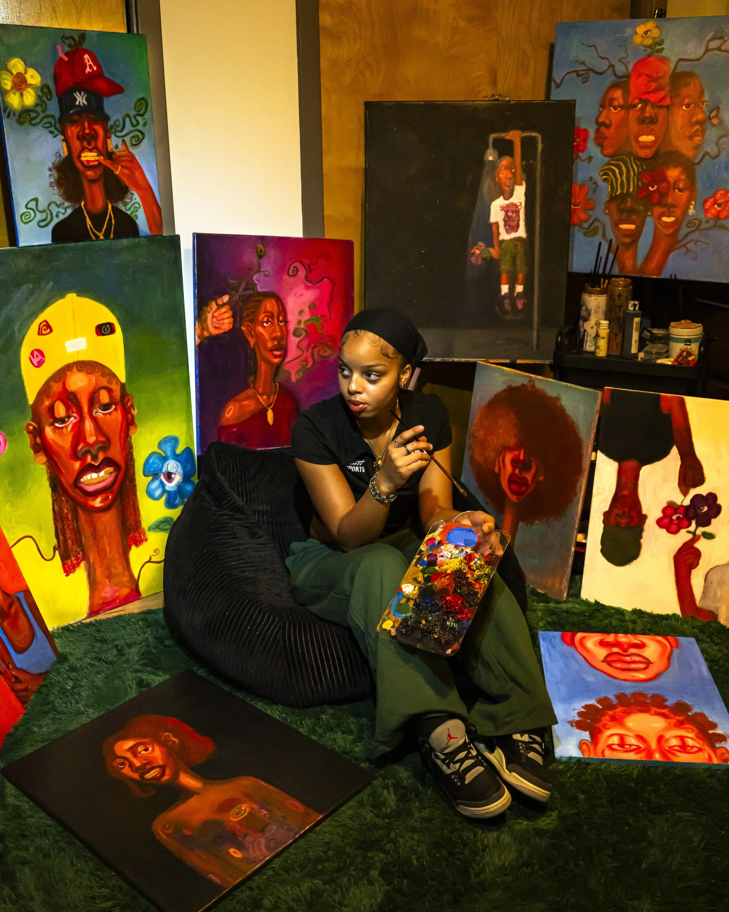 Young woman sitting among colorful paintings of African American faces at an art exhibit.