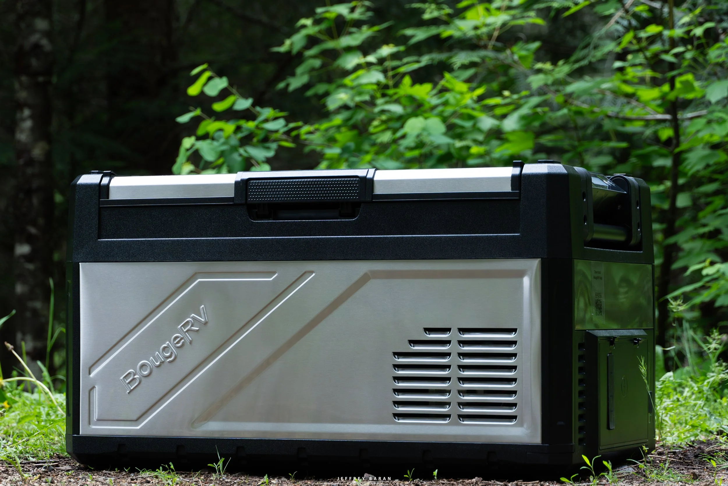 Close-up of a portable outdoor generator surrounded by green foliage in a forest setting.