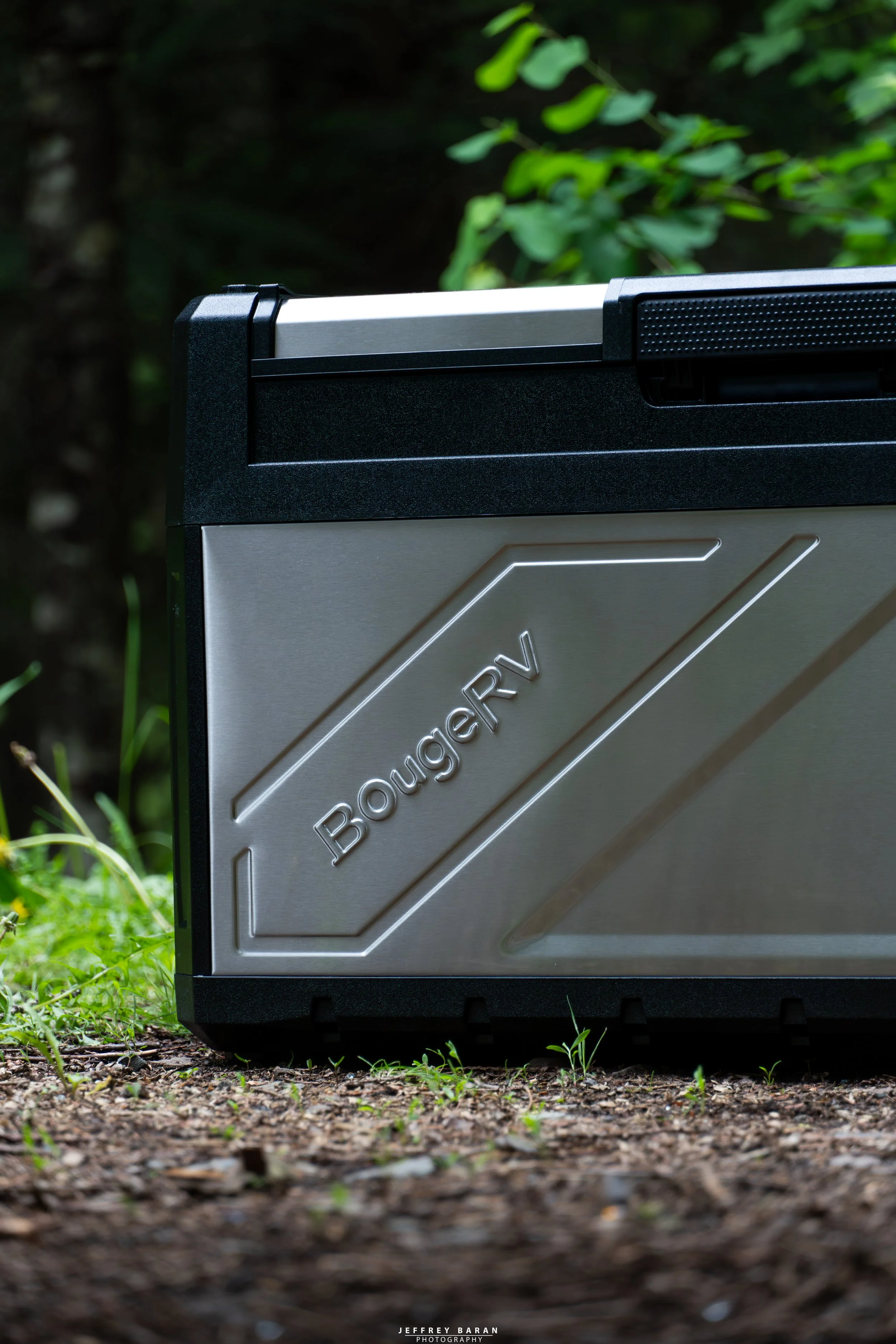 A close-up of a silver and black computer case with the word "Bonger" engraved on it, set outdoors among green grass and soil.