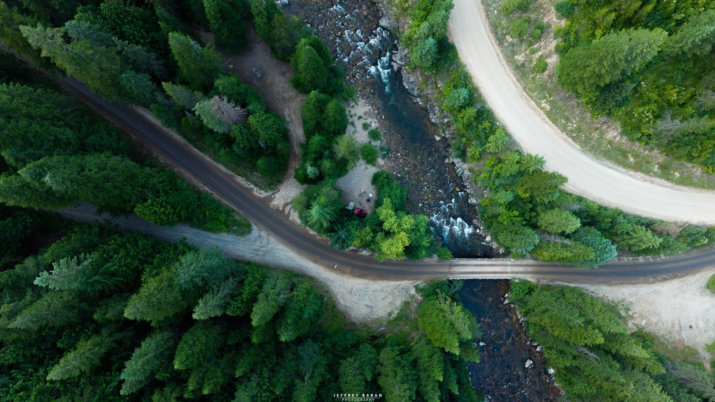 An aerial view of a forested area with a river flowing through it, surrounded by dirt roads and trees.