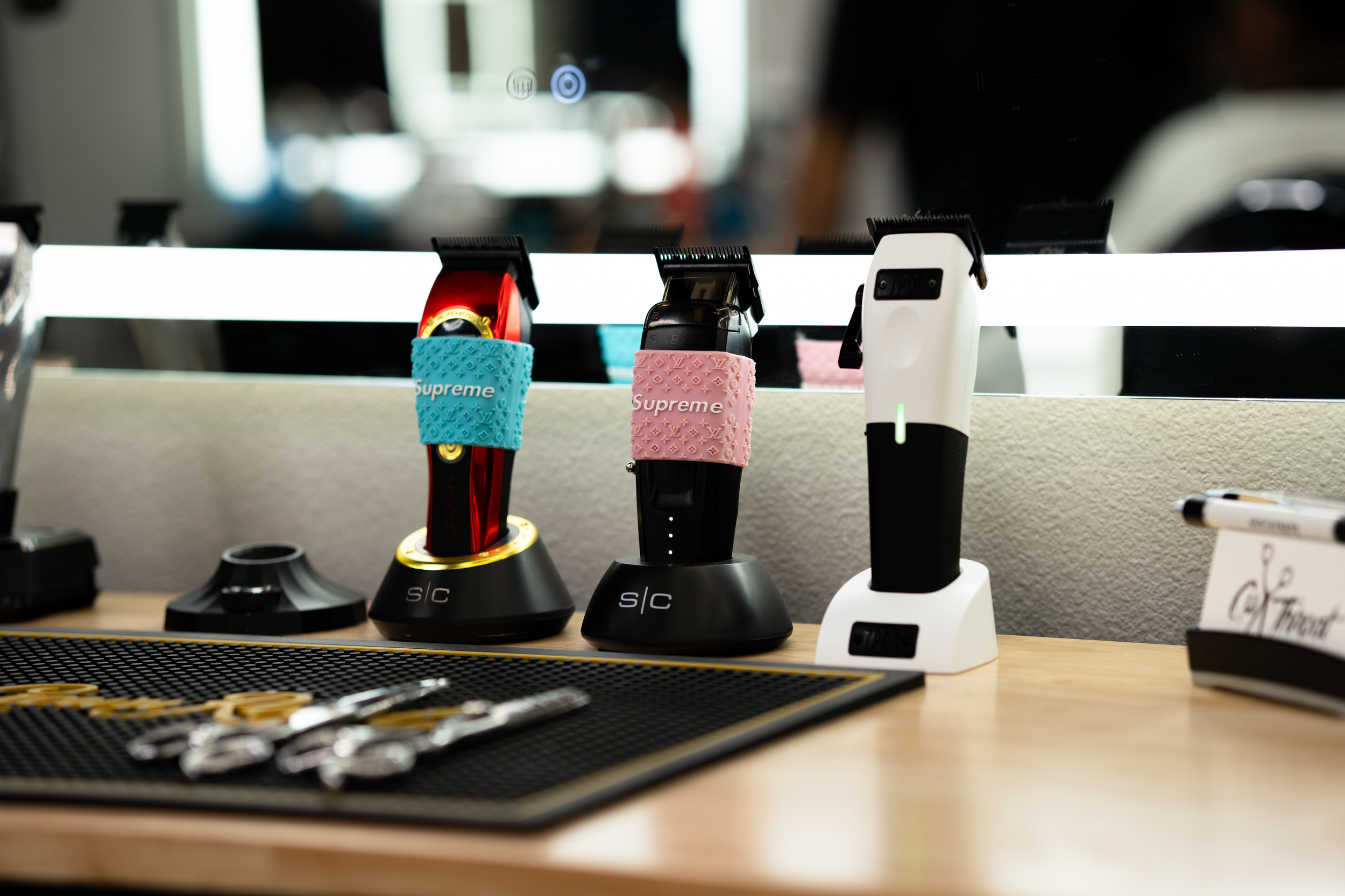 Electric hair clippers on display, some with colorful grips, sitting on a black stand in a store or salon setting.