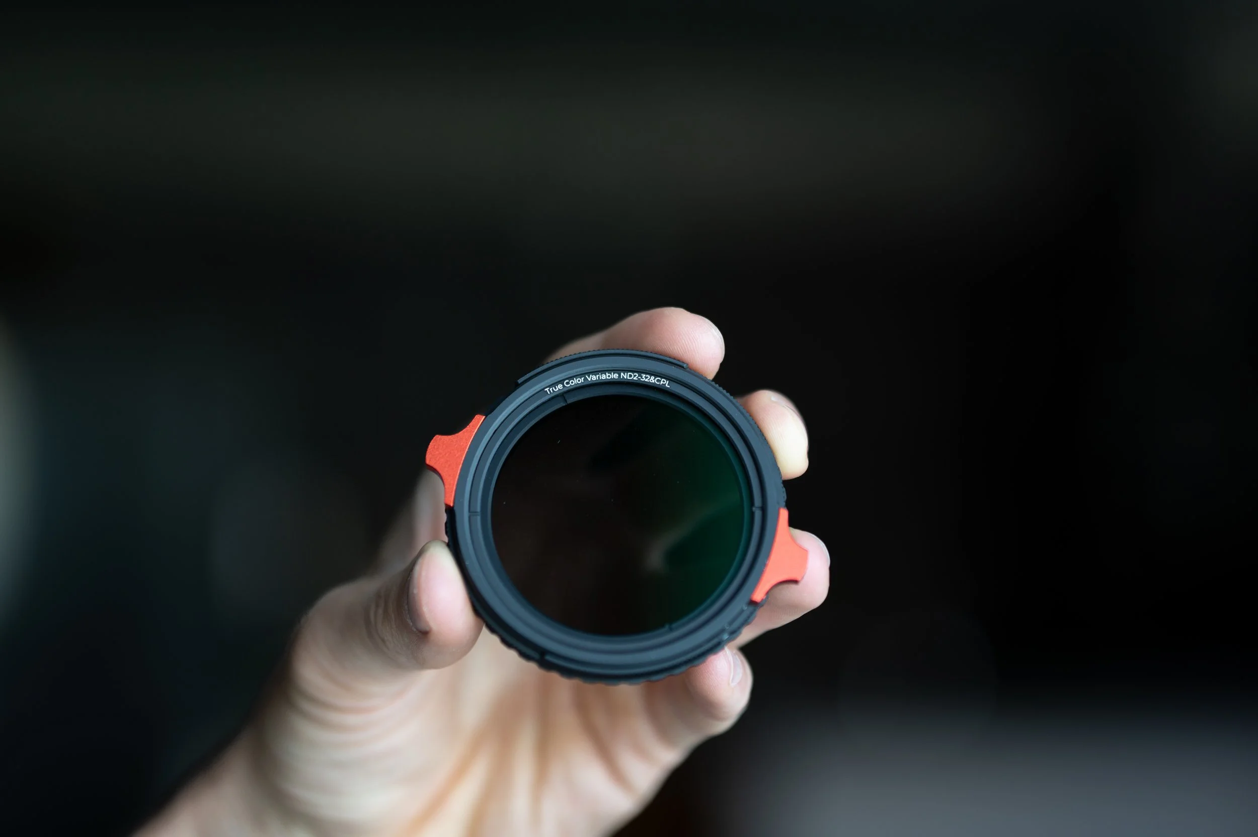 Hand holding a camera lens with a black background.